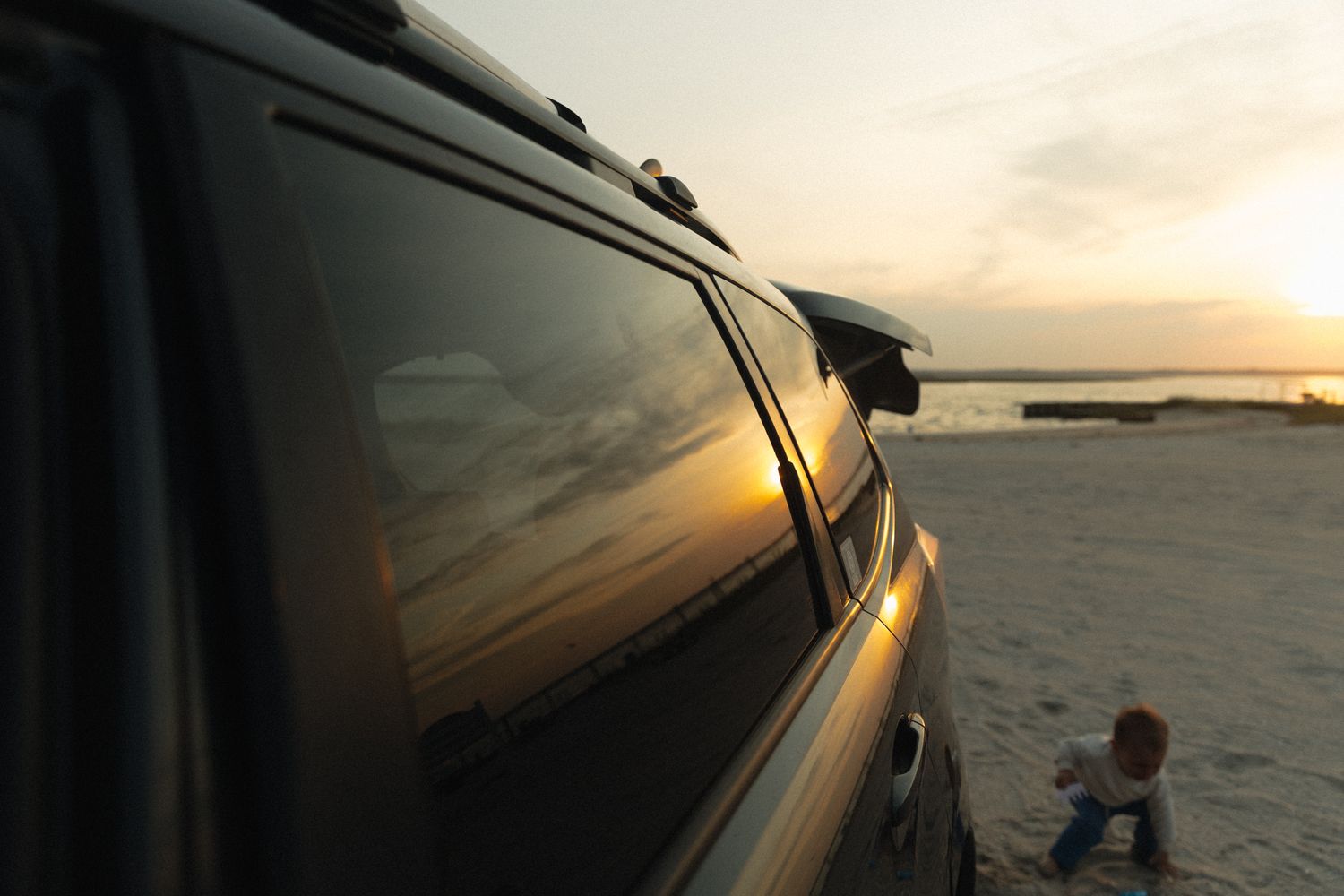 Sunset reflection in car window at beach with silhouette in background.