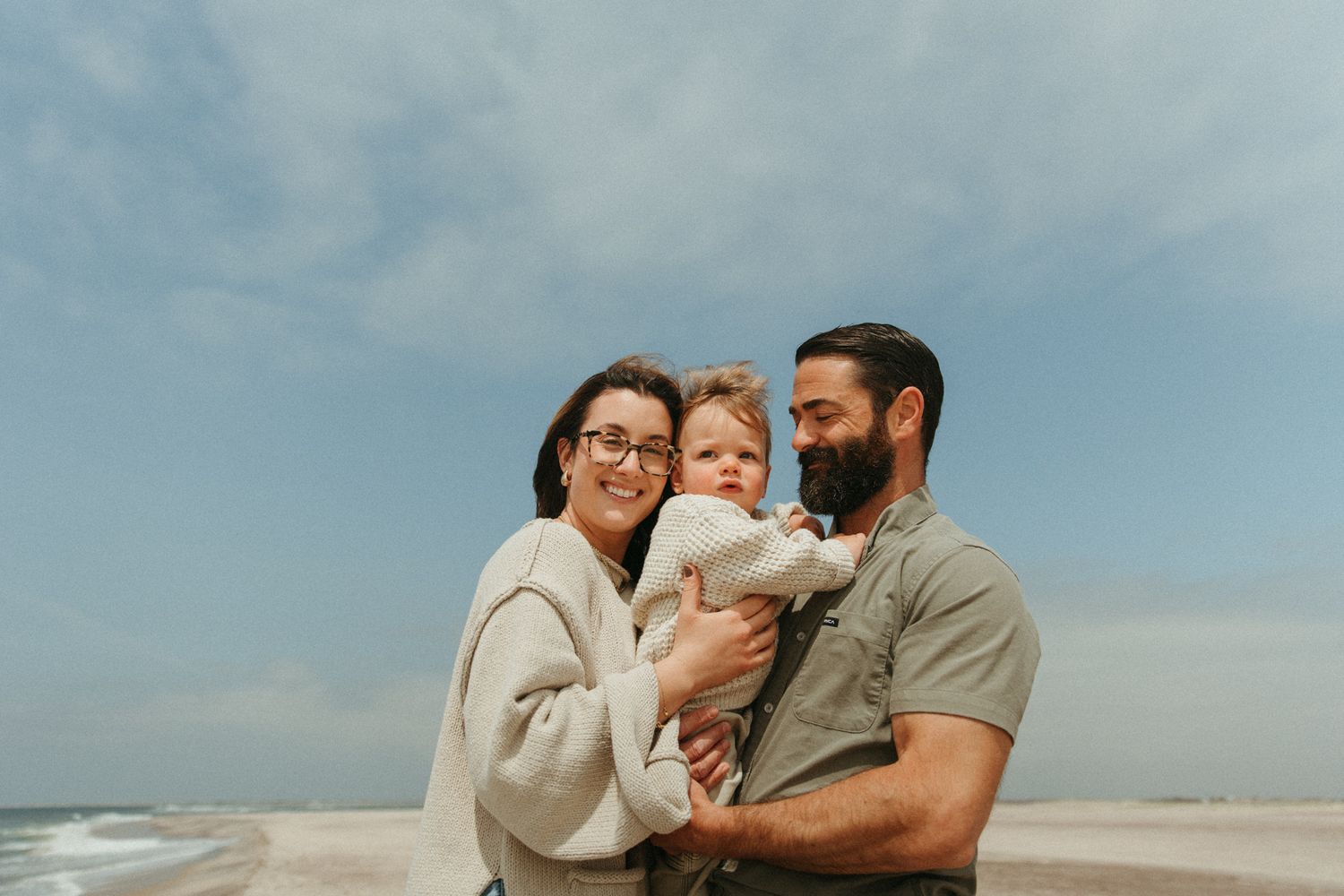 Family embracing together on a sunny beach with ocean waves in background.