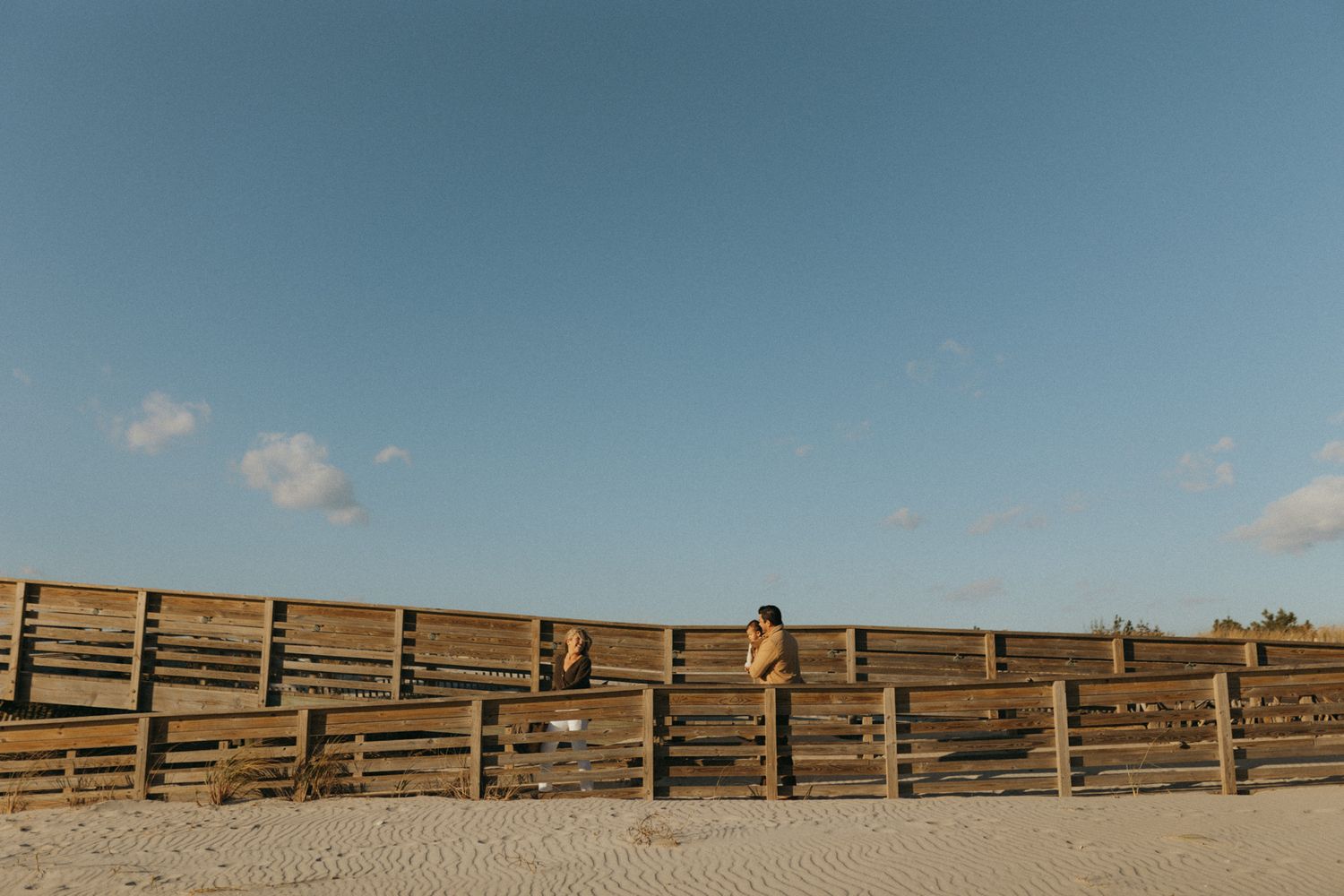 A wooden boardwalk stretches along a sandy beach under a clear blue sky.