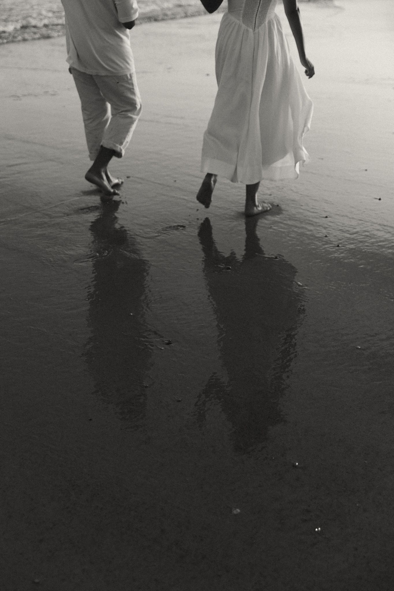Couple's feet making footprints in wet sand while dancing on a dark beach.