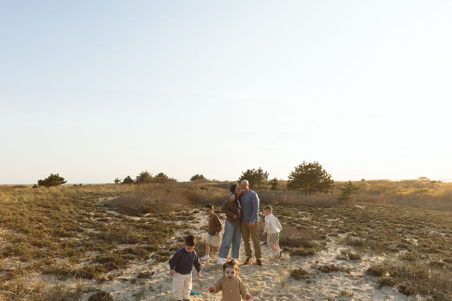 Family walking together through golden sandy dunes on a sunny day, viewed from behind.