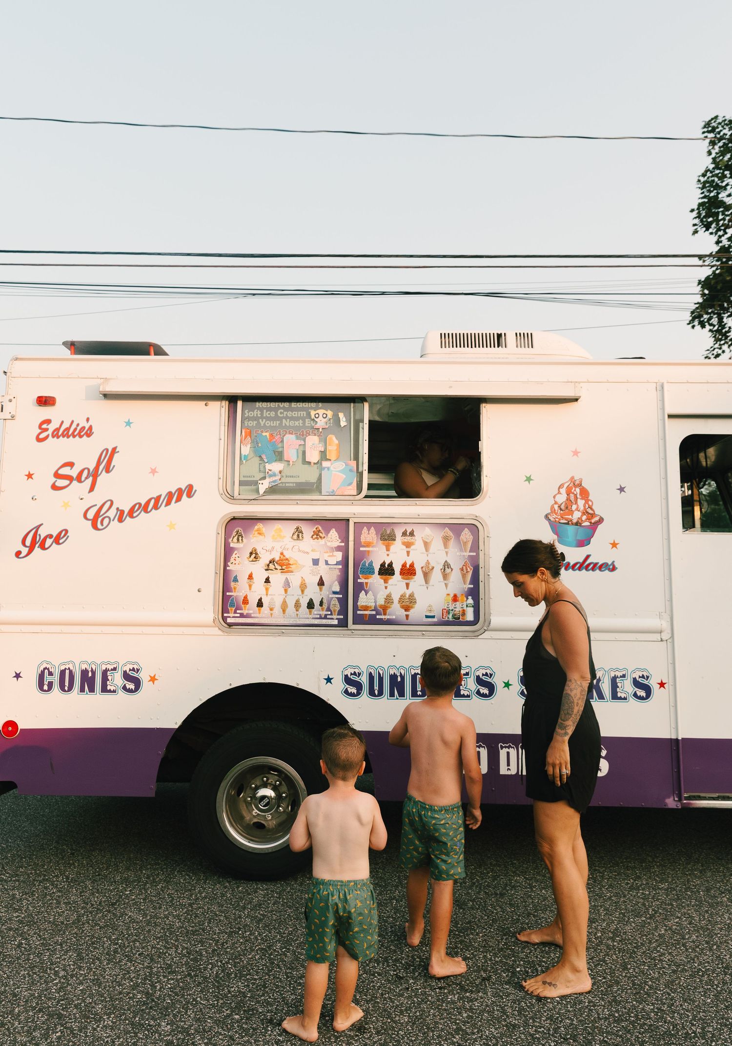 Children ordering ice cream from Eddie's Soft Ice Cream truck on a warm summer evening.