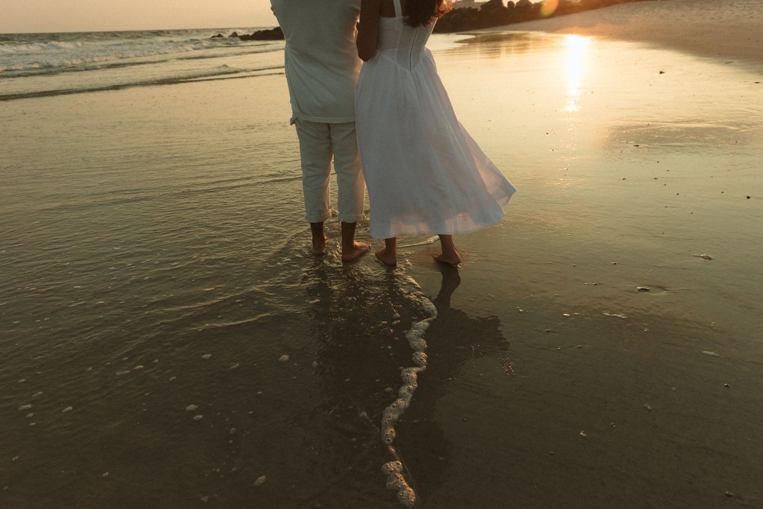 Romantic beach scene with two people walking along the shoreline during golden hour.