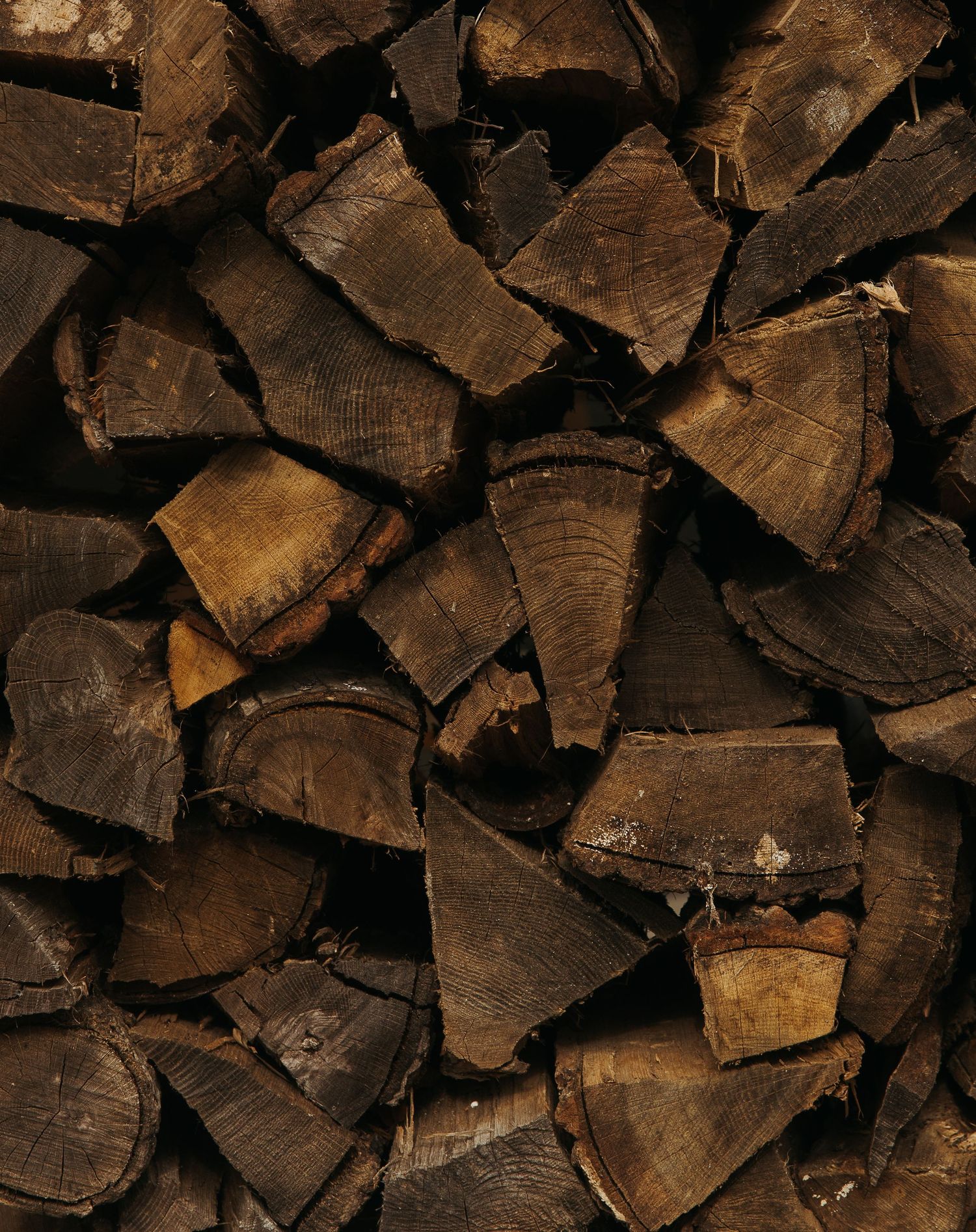 Stacked split firewood logs showing natural wood grain texture and dark brown tones, ideal for rustic or outdoor themes.