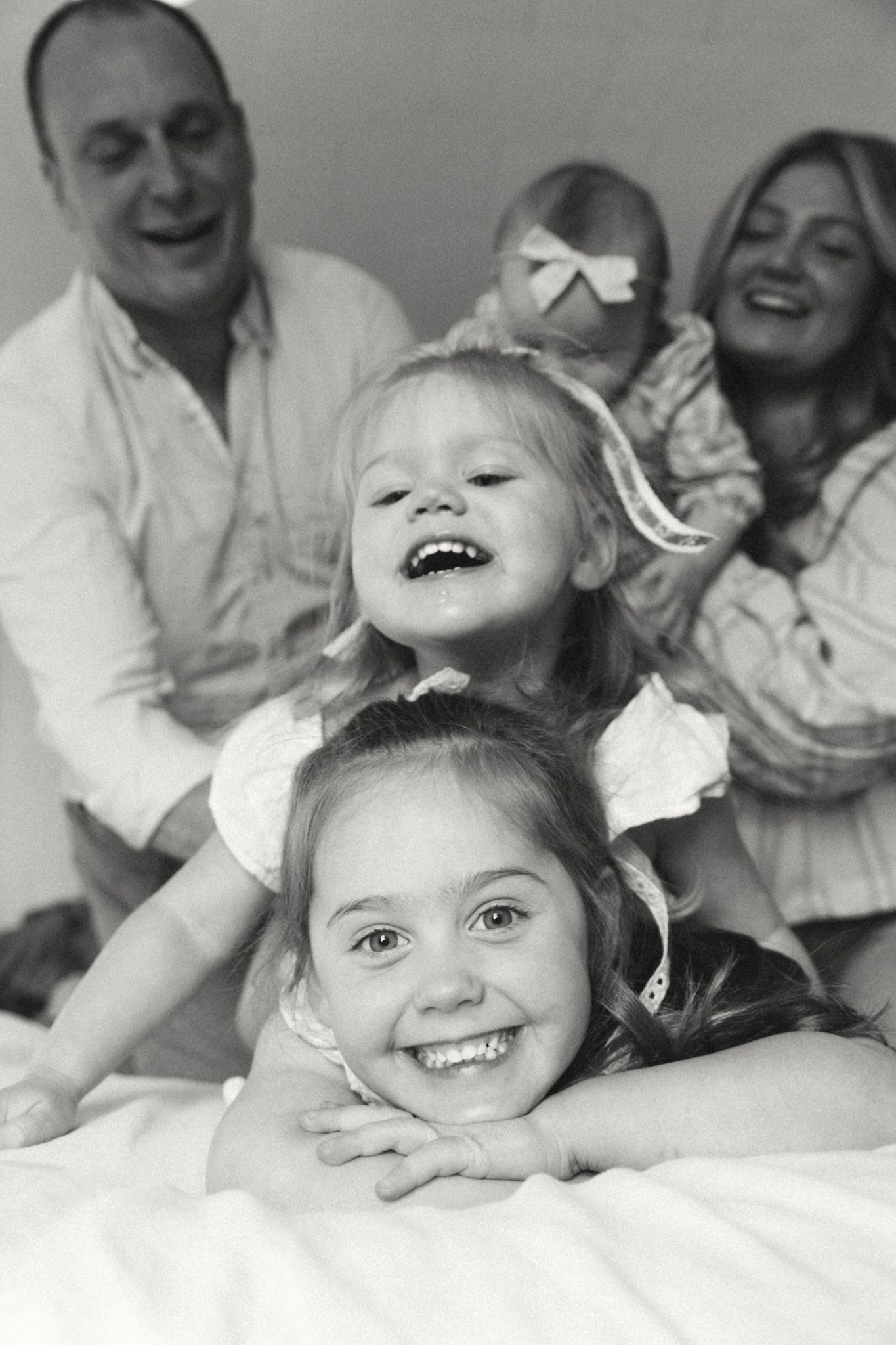 Black and white portrait of joyful family moments on white bedding.