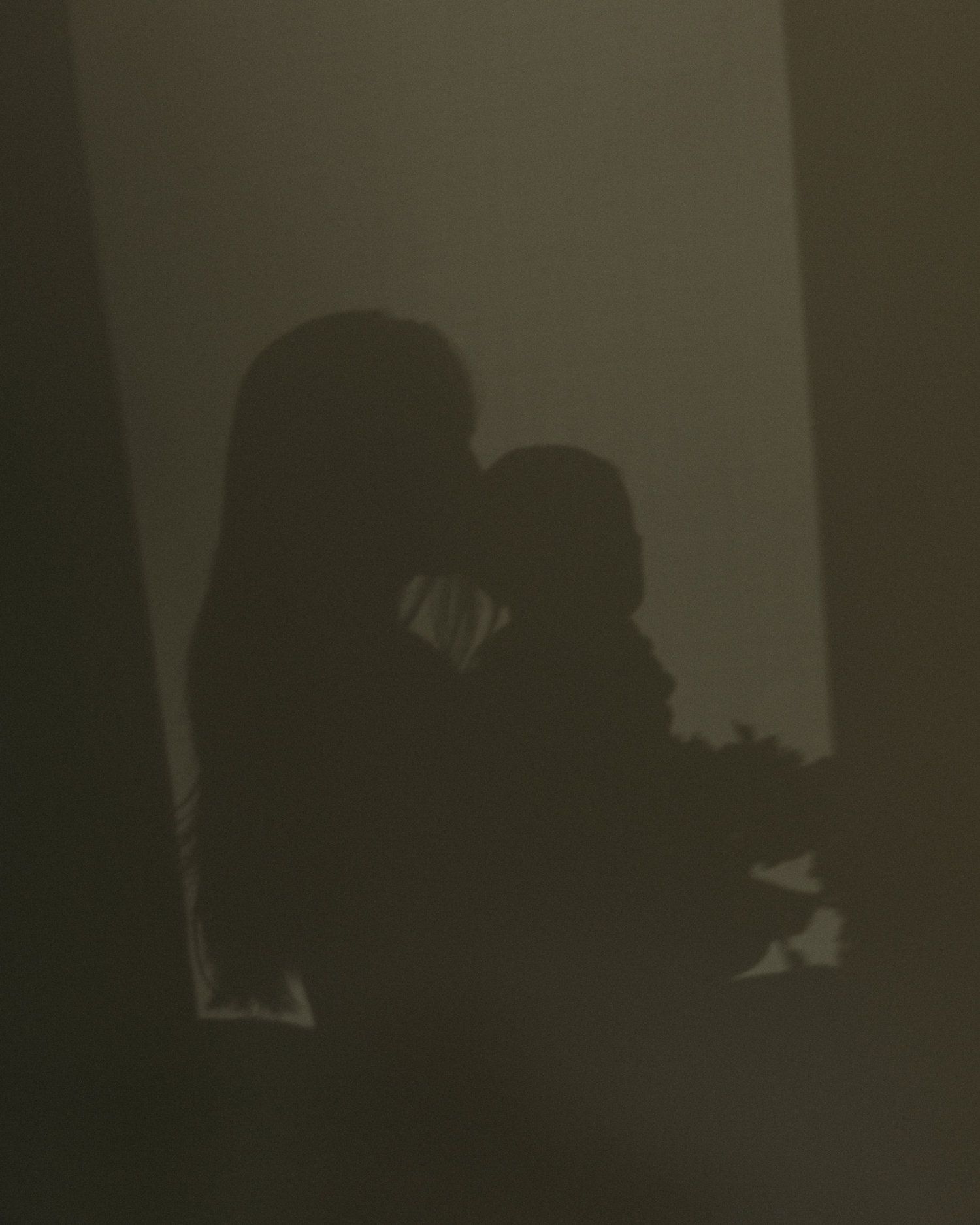 Silhouette of a mother tenderly holding her baby cast as a shadow on a dark wall.