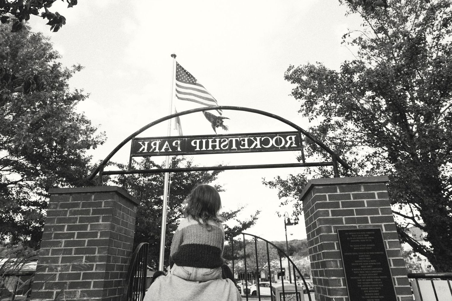 Rustic brick entrance gate with American flag flying on top during autumn.