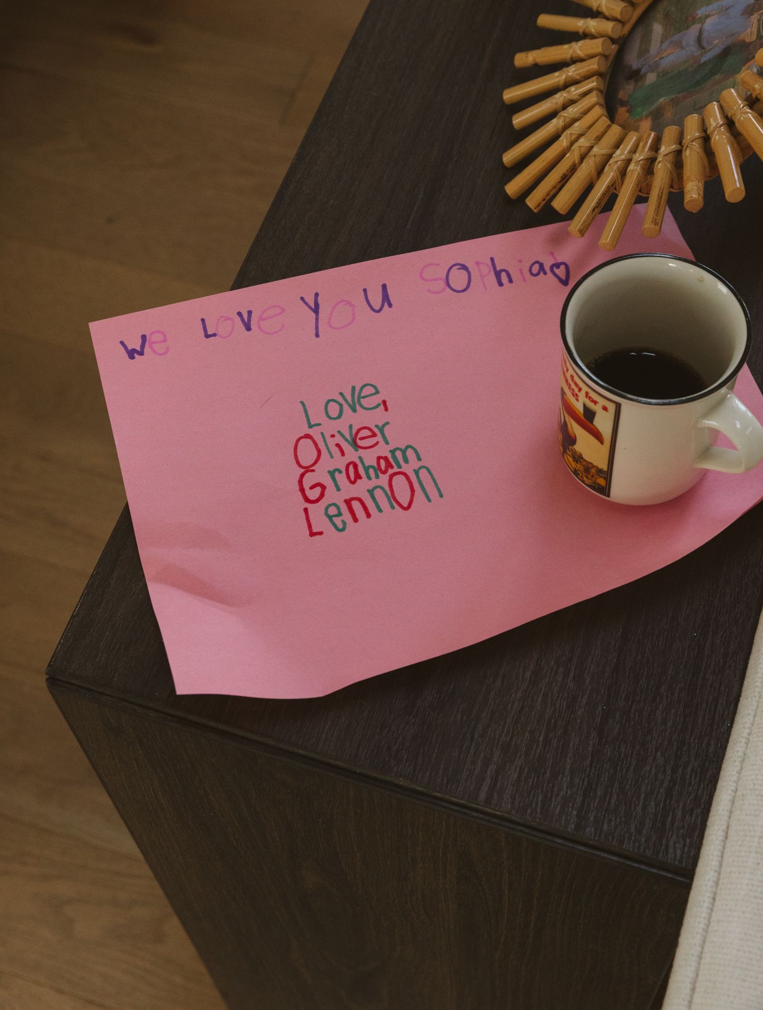 Pink love note on dark wooden table with coffee cup and sunburst decoration.