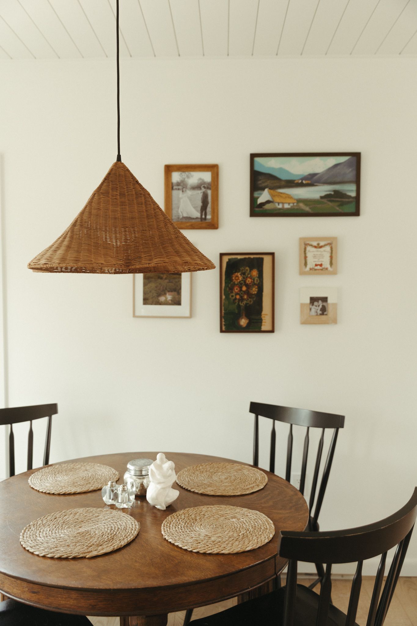 Dining room with round wooden table, black chairs, and woven pendant lamp.
