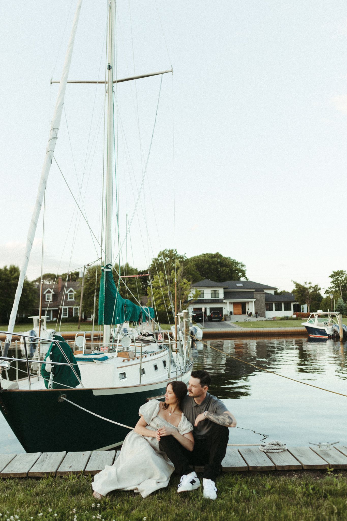 A couple relaxing on grass near docked sailboats in a marina.