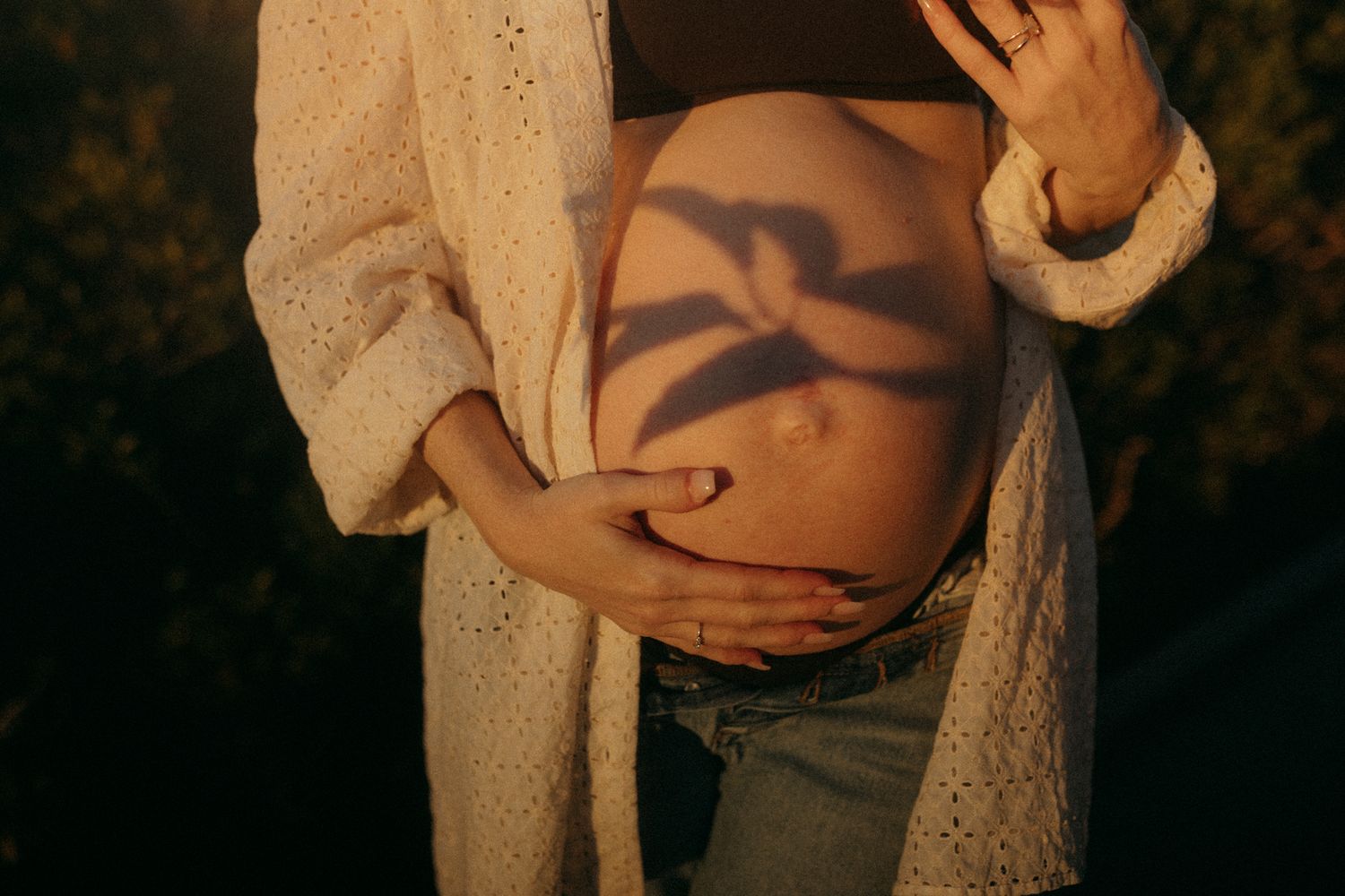 Intimate maternity photoshoot with white lace dress in natural lighting.