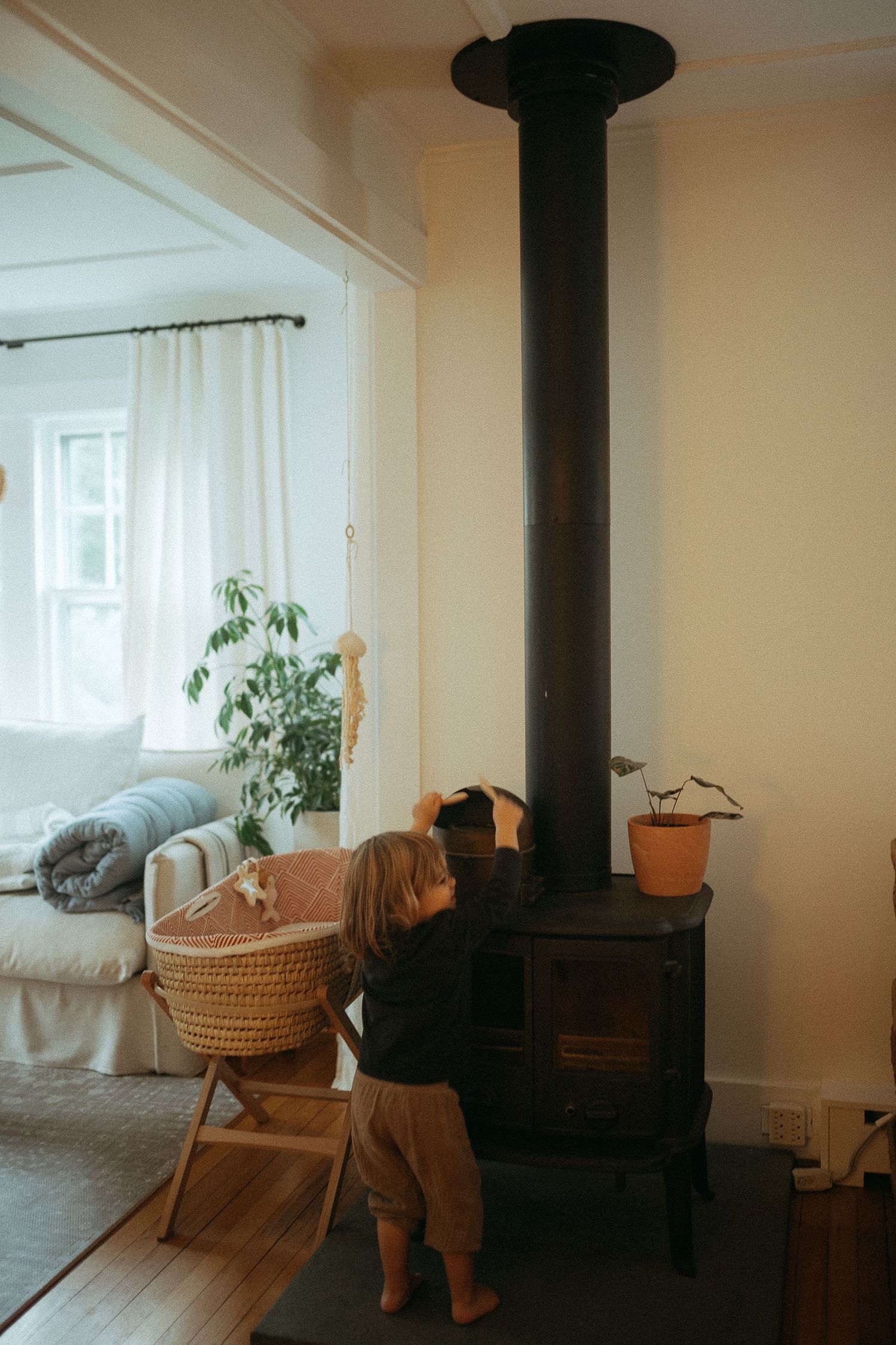 Cozy living room with wood stove, wicker furniture, and white curtains in natural light.
