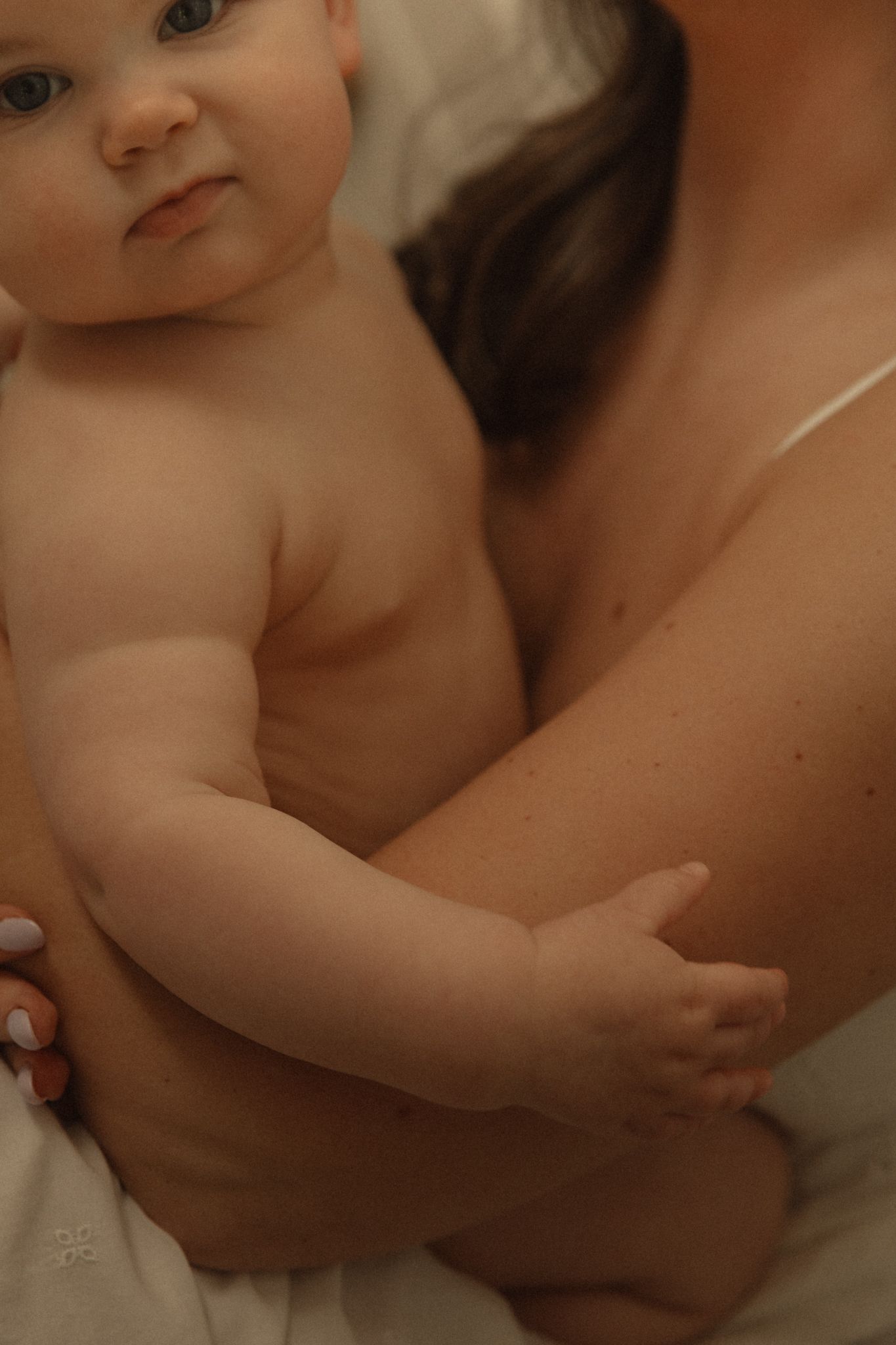 Close-up of chubby newborn baby being cradled in mothers arms against soft white background.