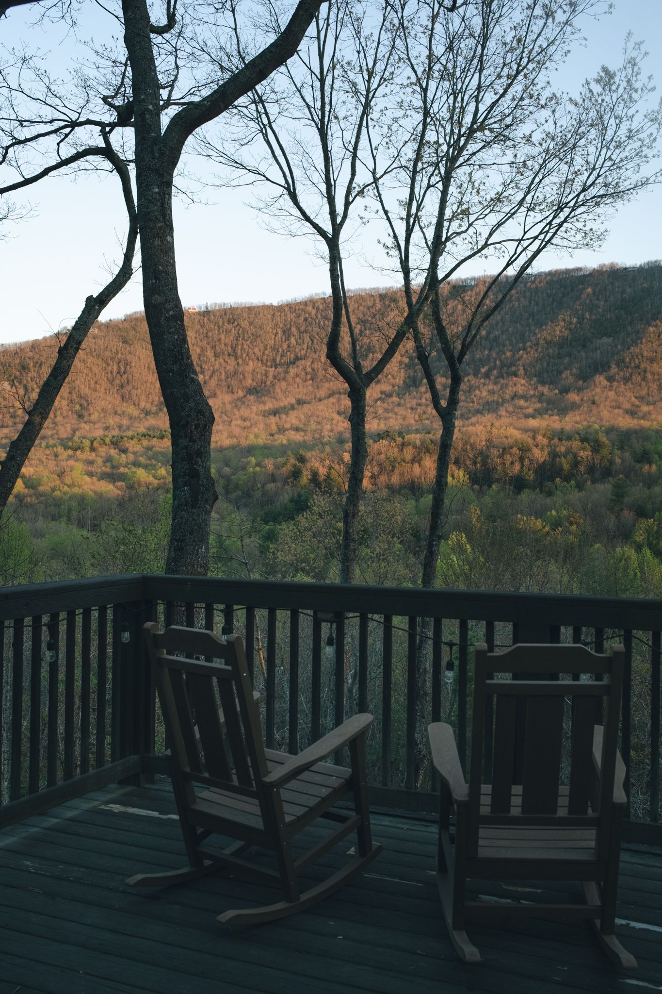 Two wooden rocking chairs on a deck overlooking autumn mountain forest views at dusk.