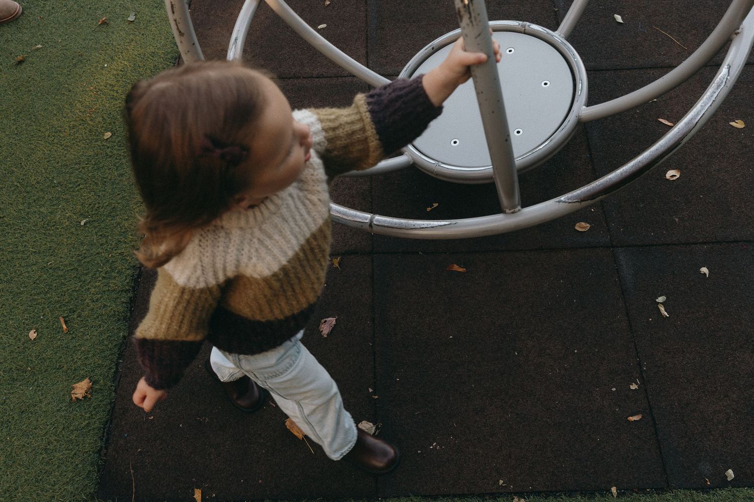 Someone in a brown sweater plays on outdoor playground equipment.