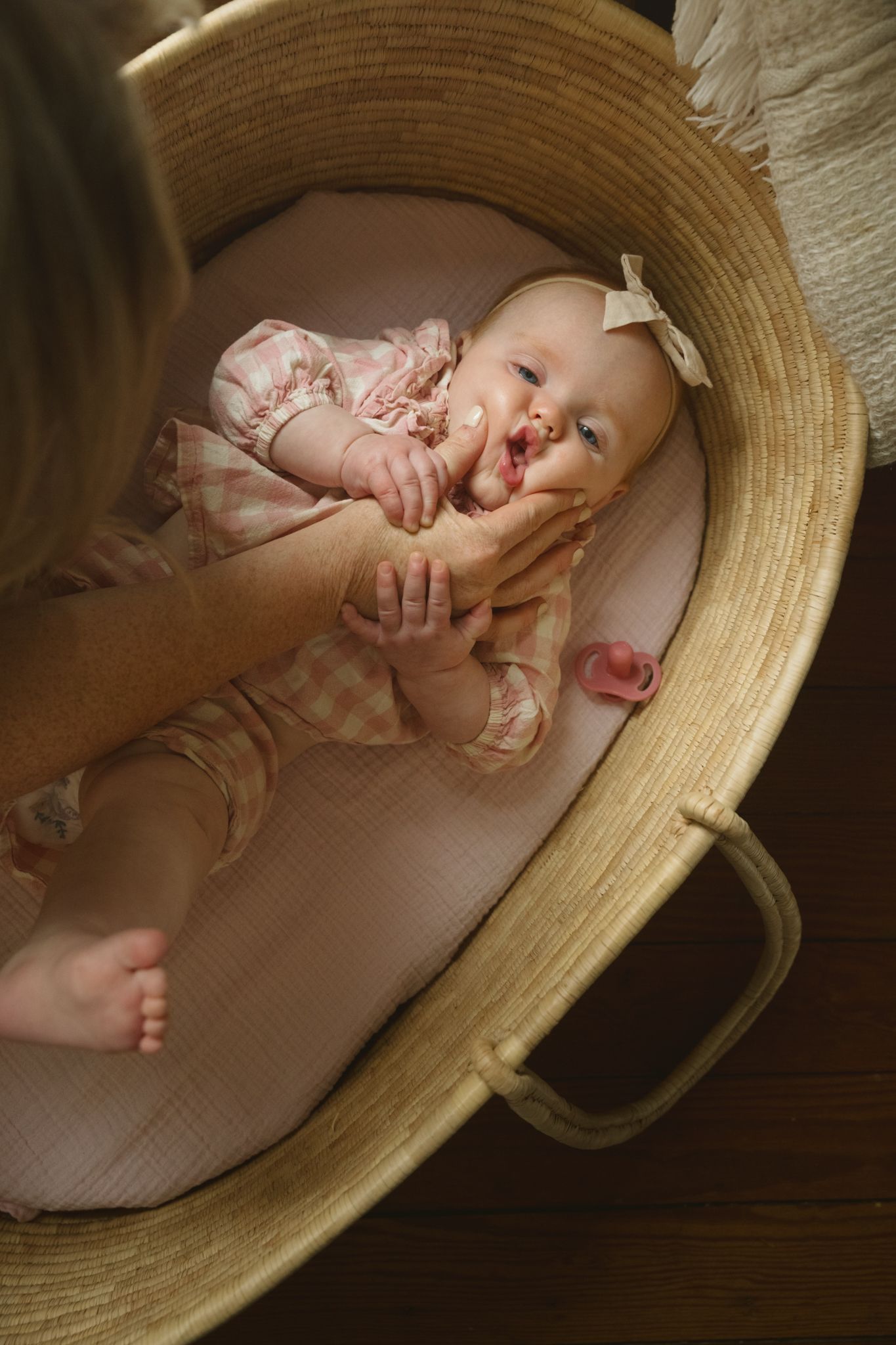 Baby lying in a woven moses basket with soft pink bedding.