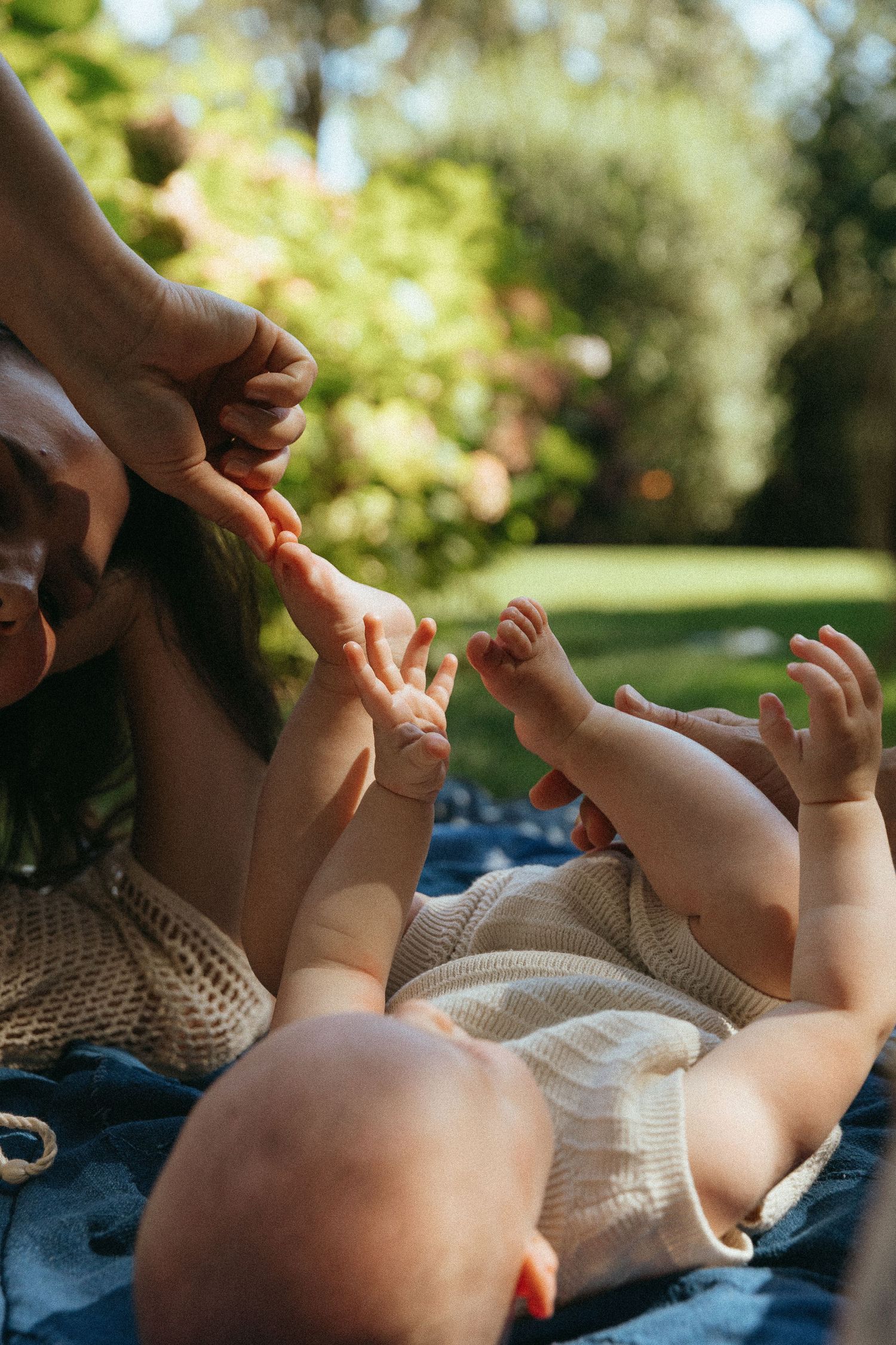 Baby feet being tickled during outdoor photoshoot on a sunny day.