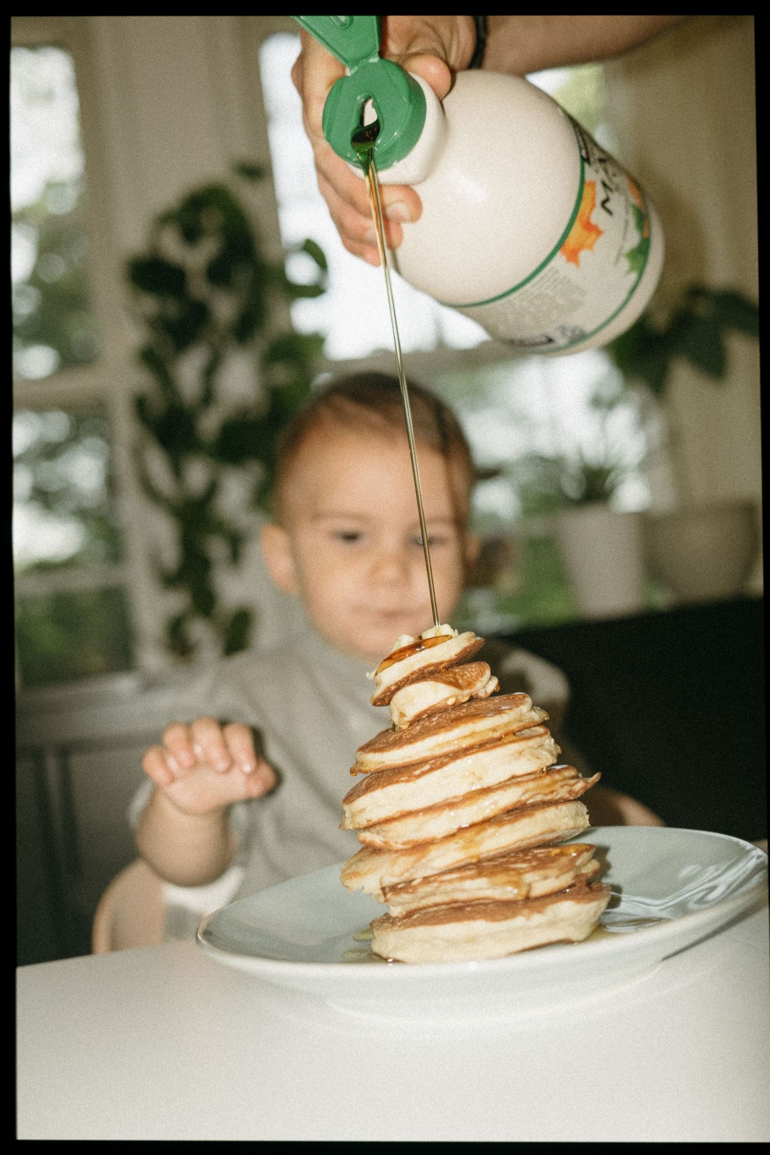 Stack of pancakes being drizzled with syrup on white plate.