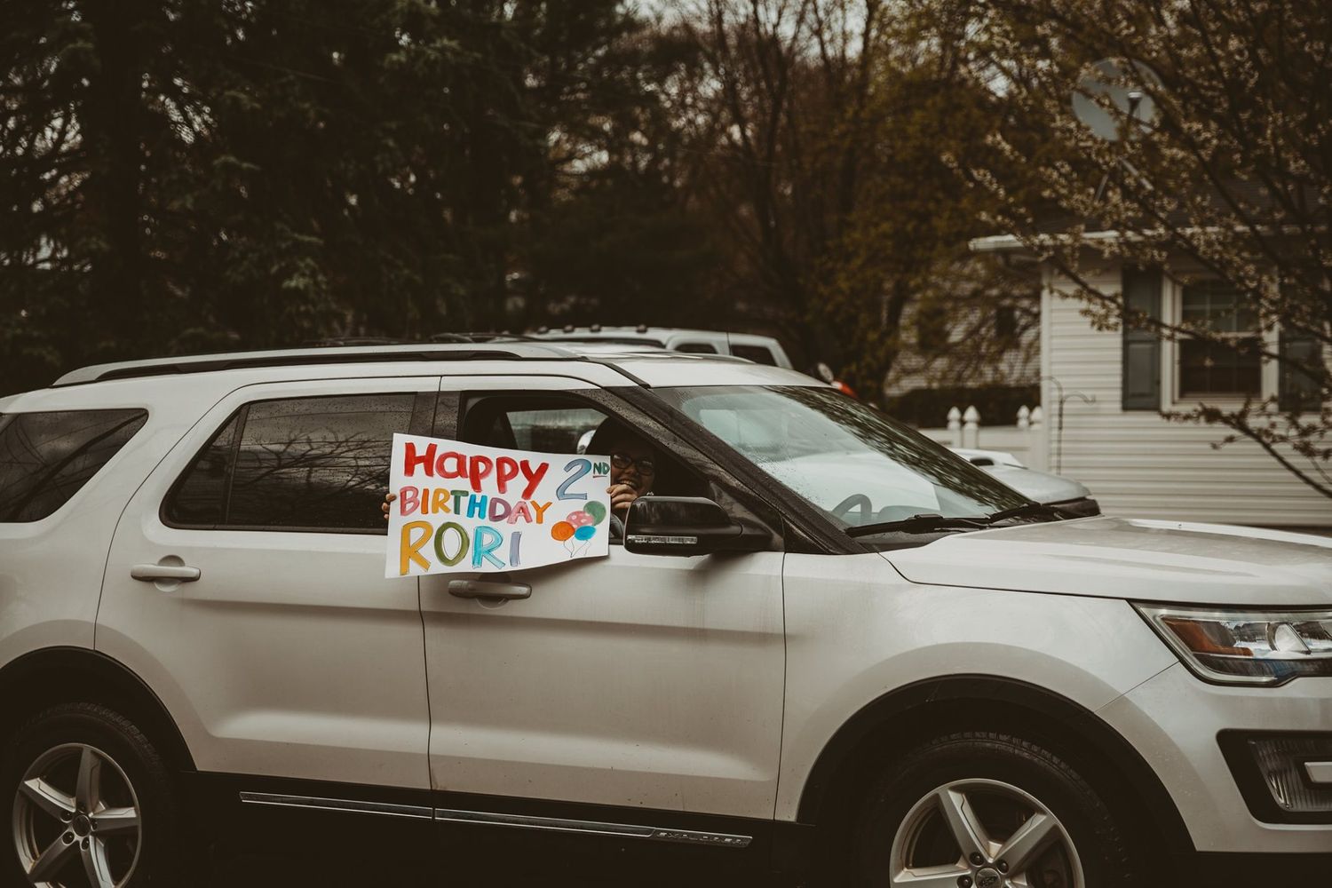 Cars with birthday signs and decorations form a parade line on a residential street.