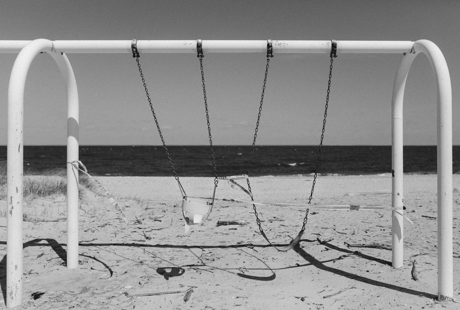 Empty metal swing set frames stand against a stark desert landscape in black and white.