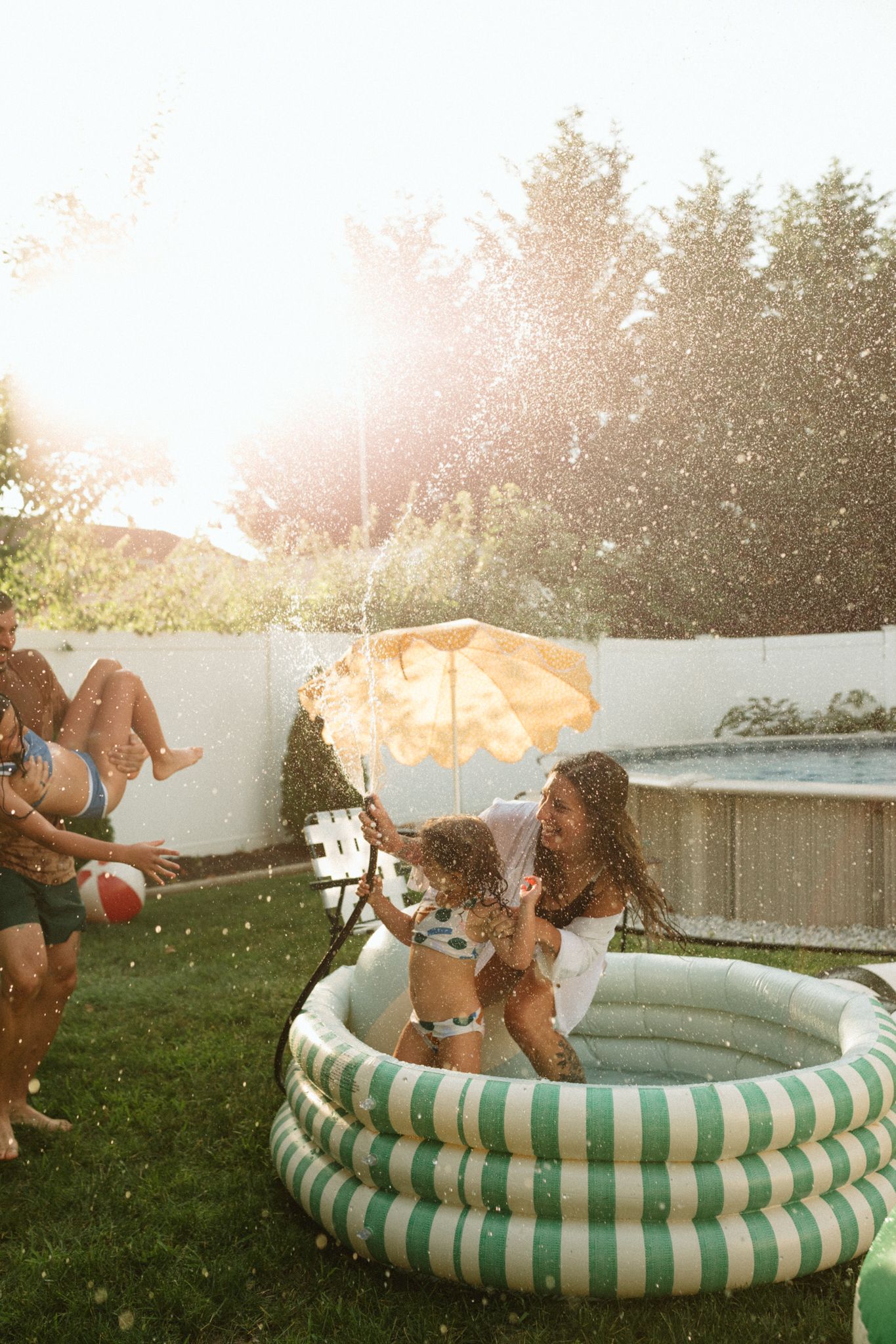 Summer pool party scene with inflatable pool and water splashing in golden sunlight.