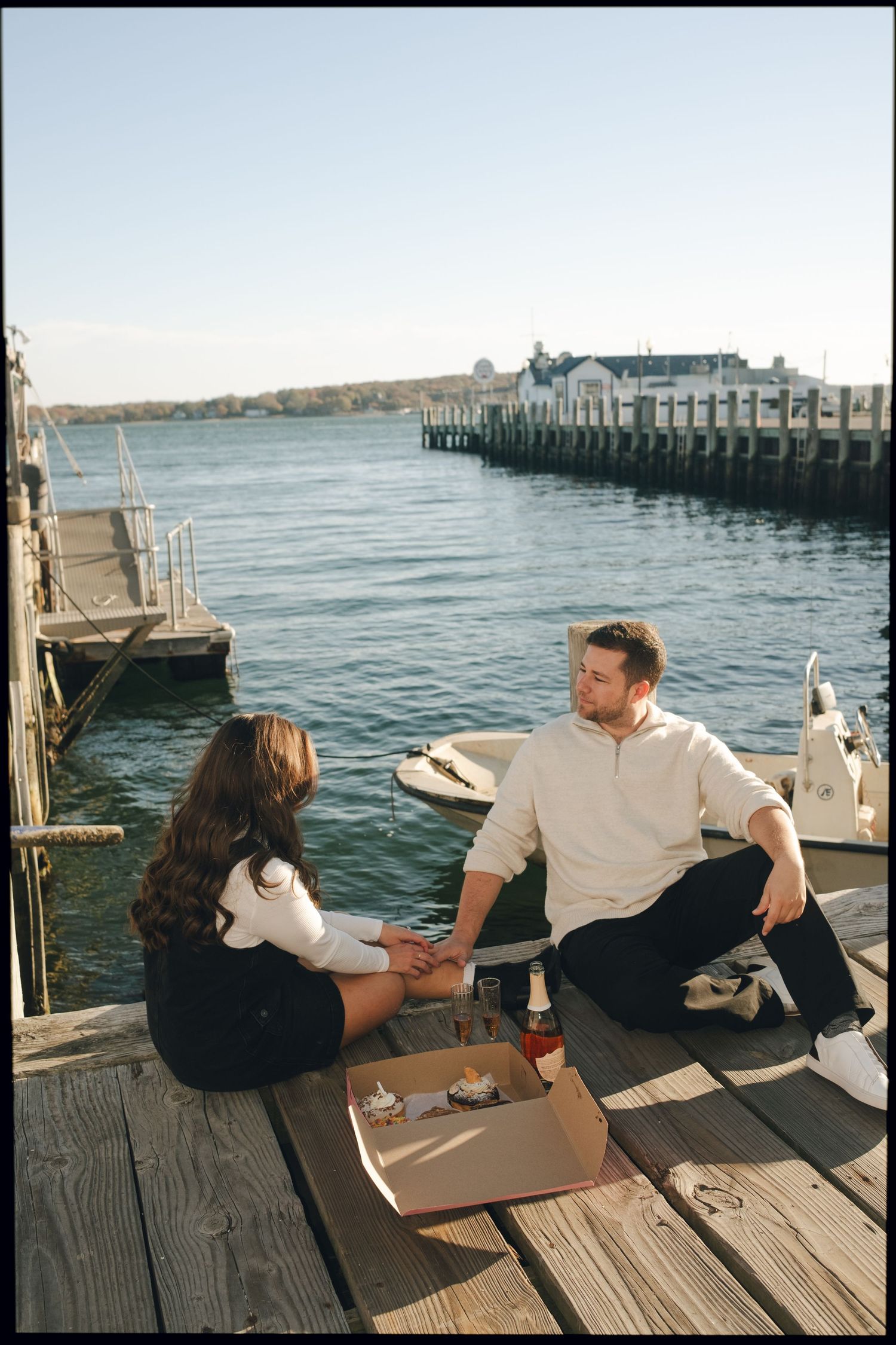 Couple relaxing together on a wooden dock by the water during sunset.