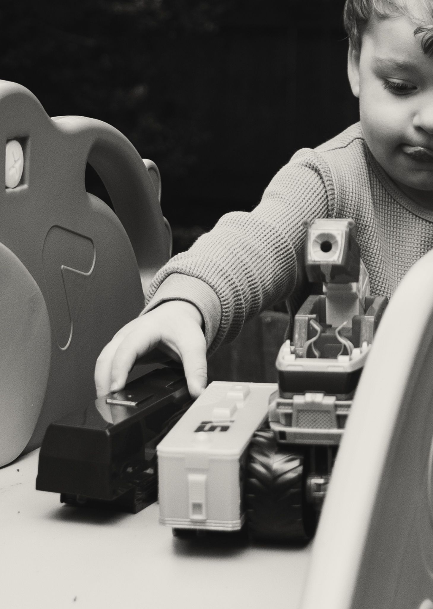 Black and white photo of a young child playing with toy trucks and vehicles on a table.