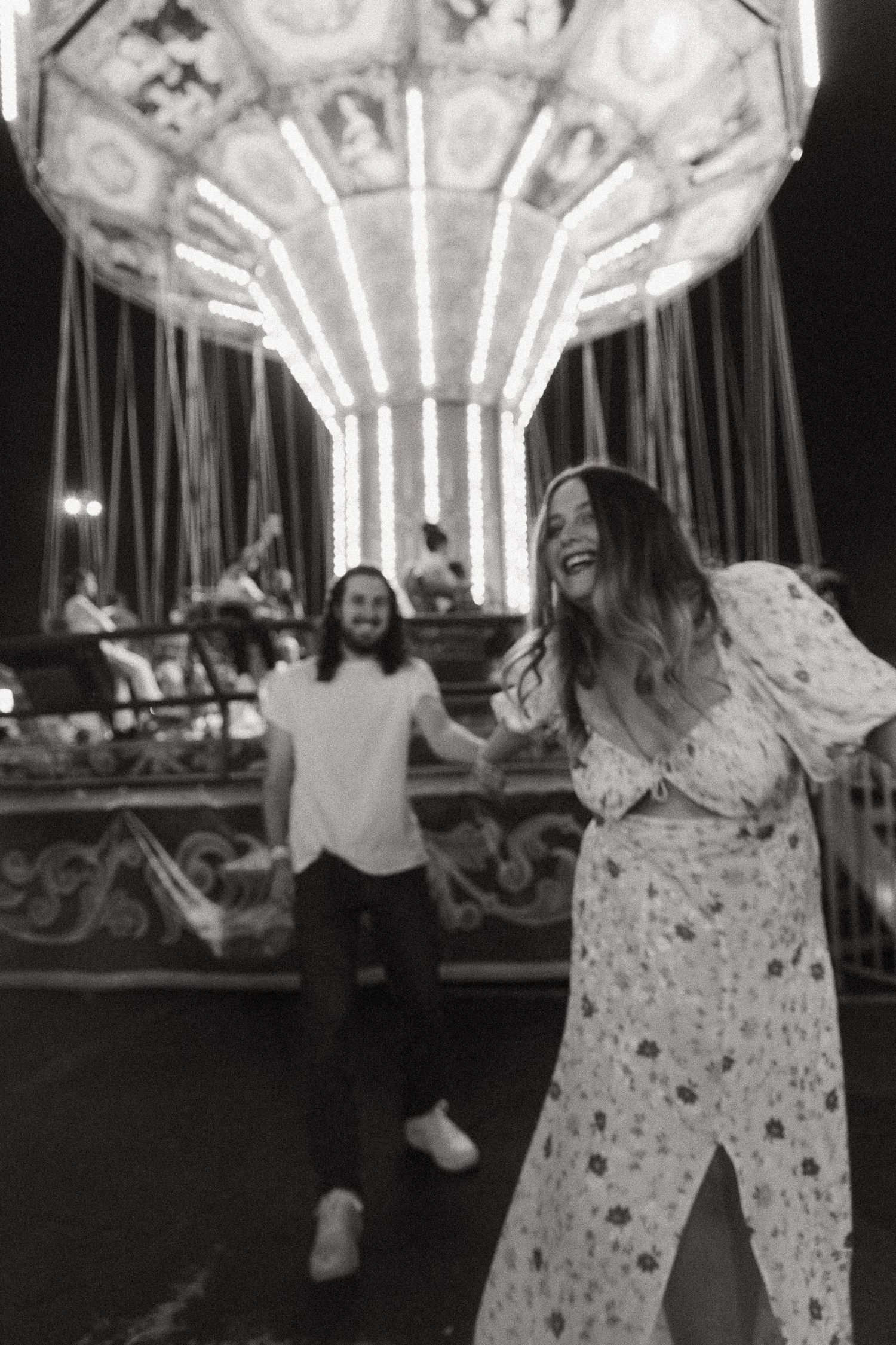 Black and white photo of a laughing couple at a carnival with a lit carousel in the background at night.