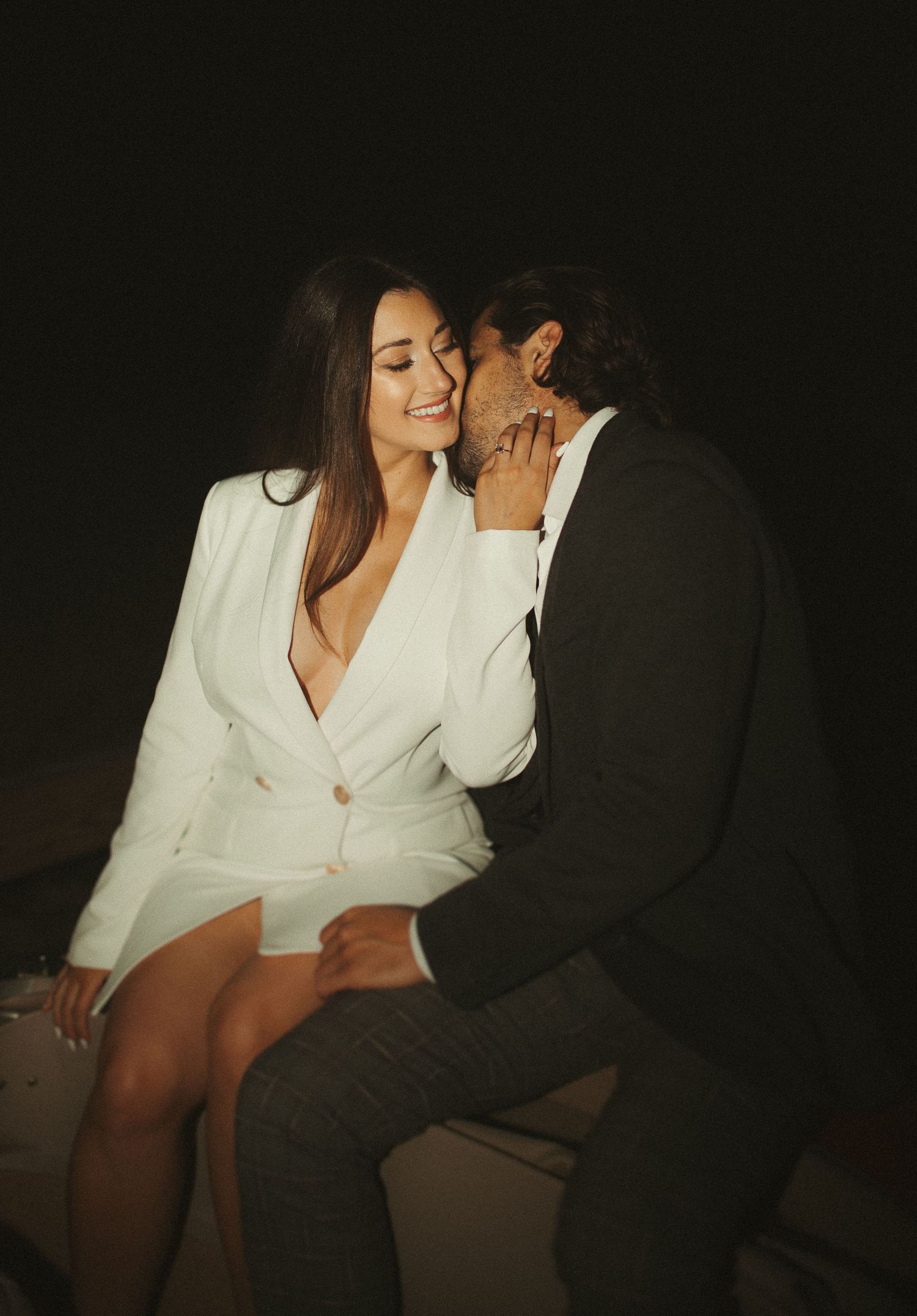 Intimate couple portrait against dark background in formal attire.