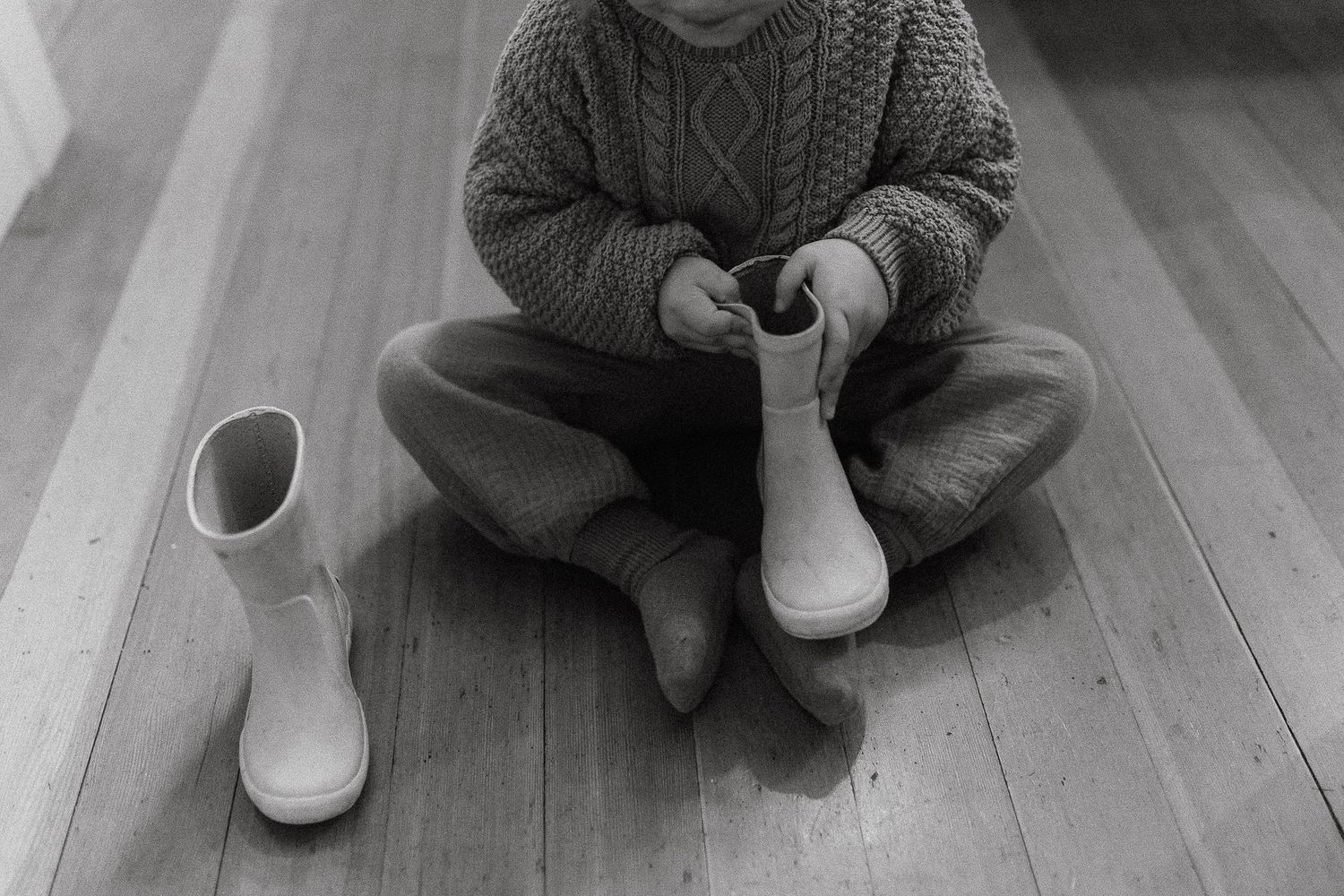 Person wearing gray knit sweater sitting on wooden floor.