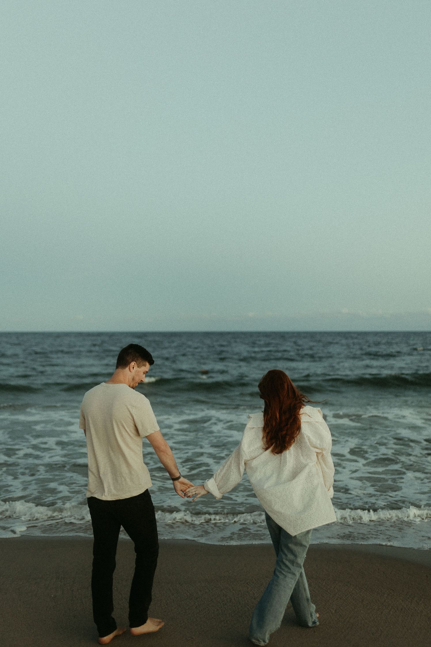 Two people dance together on a sandy beach with the ocean waves in the background.