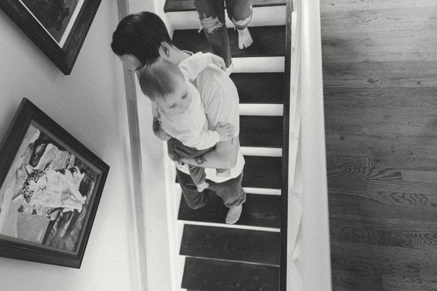 Black and white photograph showing stairs with framed artwork on the wall.