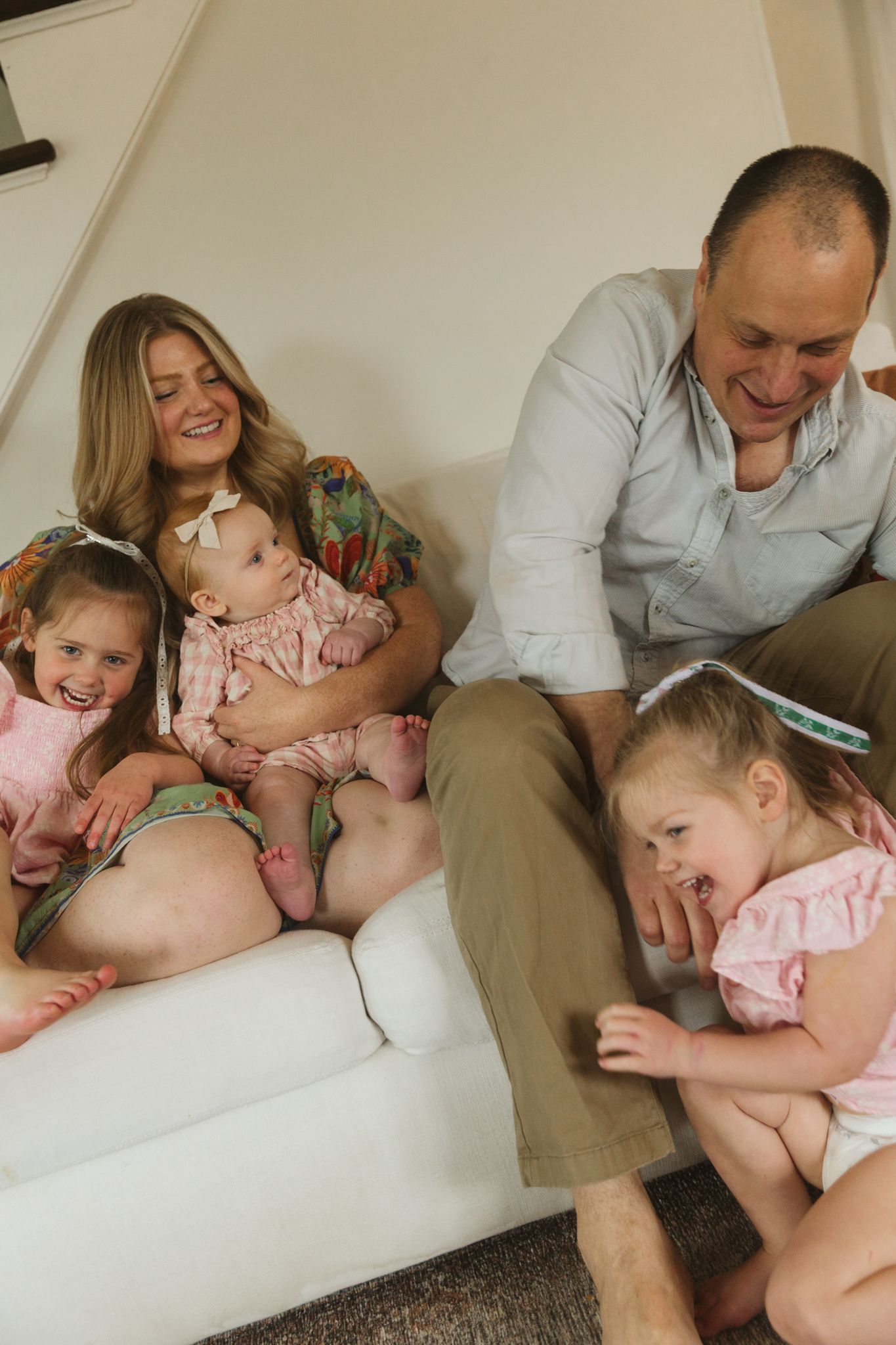 A joyful family moment captured on a white couch with everyone laughing together.