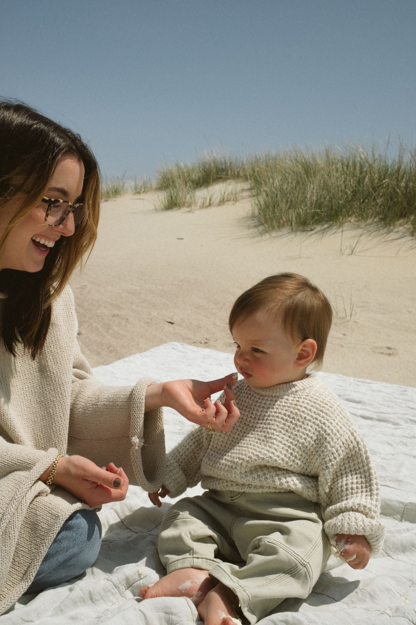 Candid moments of family interaction on a beach blanket with coastal dunes in the background.