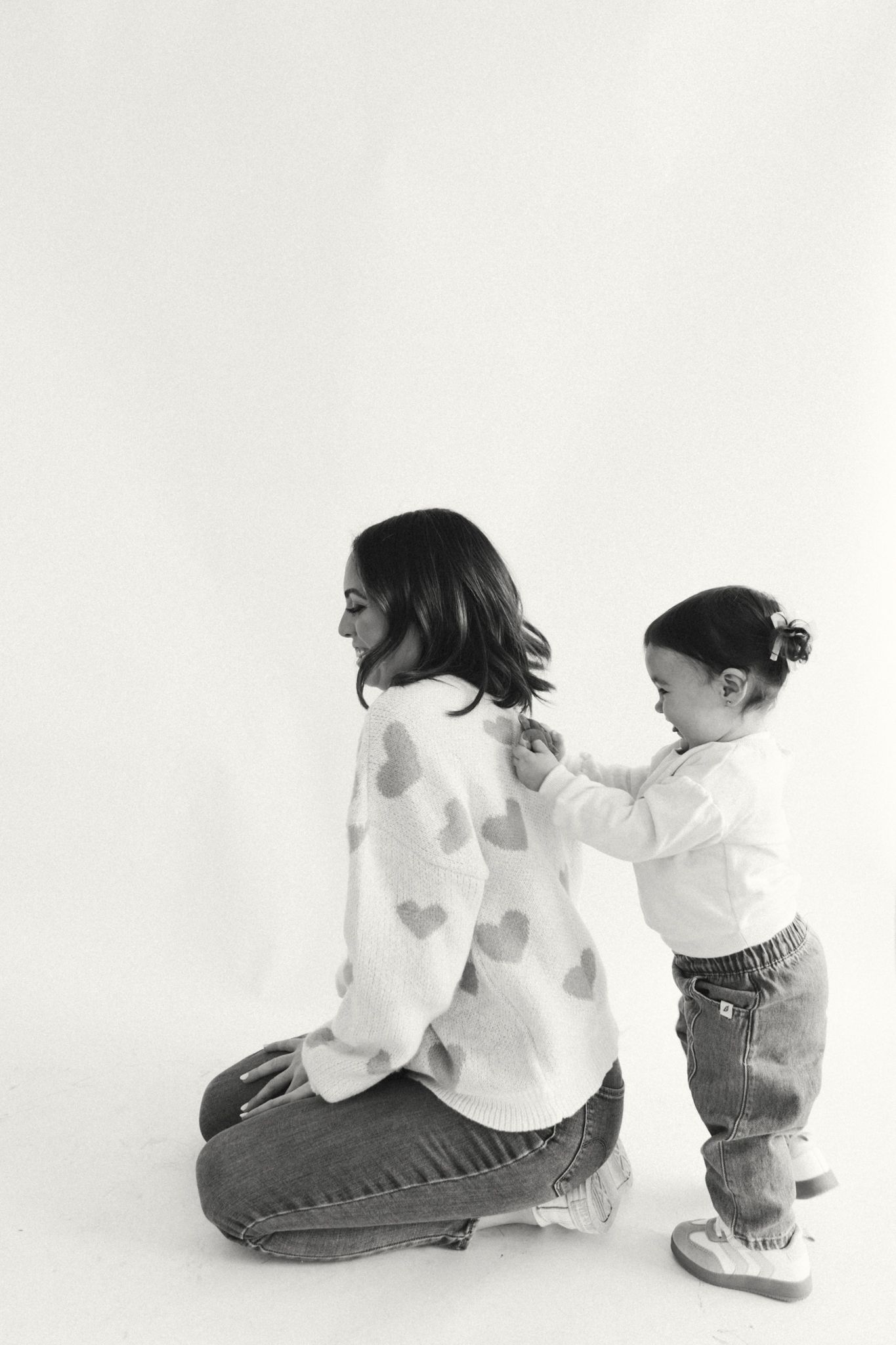 Two people in white shirts and jeans sitting and interacting on a light background.