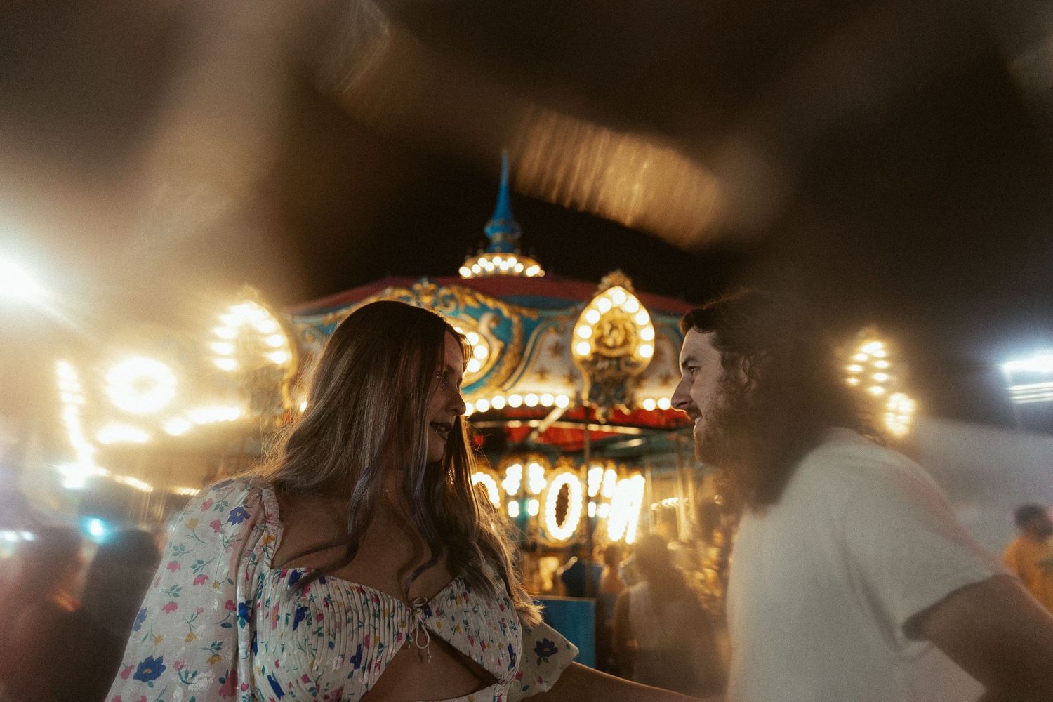 Couple sharing an intimate moment at a colorful illuminated carnival ride at night.