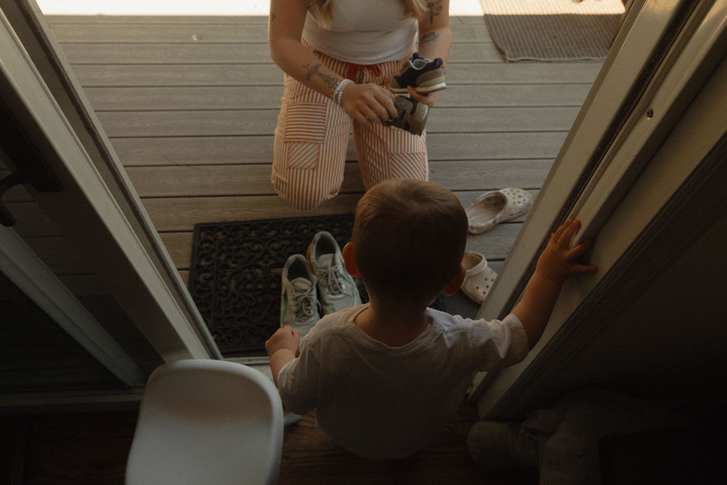 Overhead view of a woman and young child playing near a doorway on a wooden porch at golden hour.