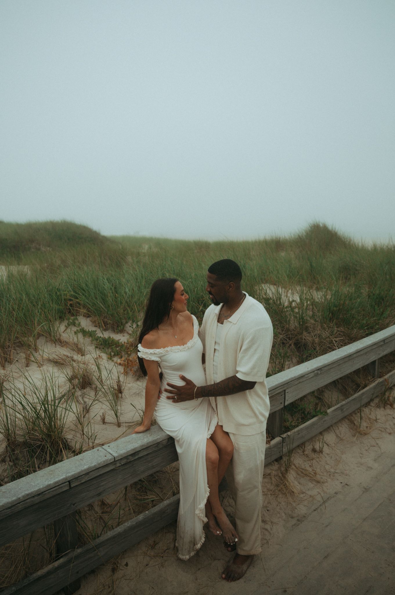 Couple sharing intimate moment on wooden boardwalk by beach dunes.