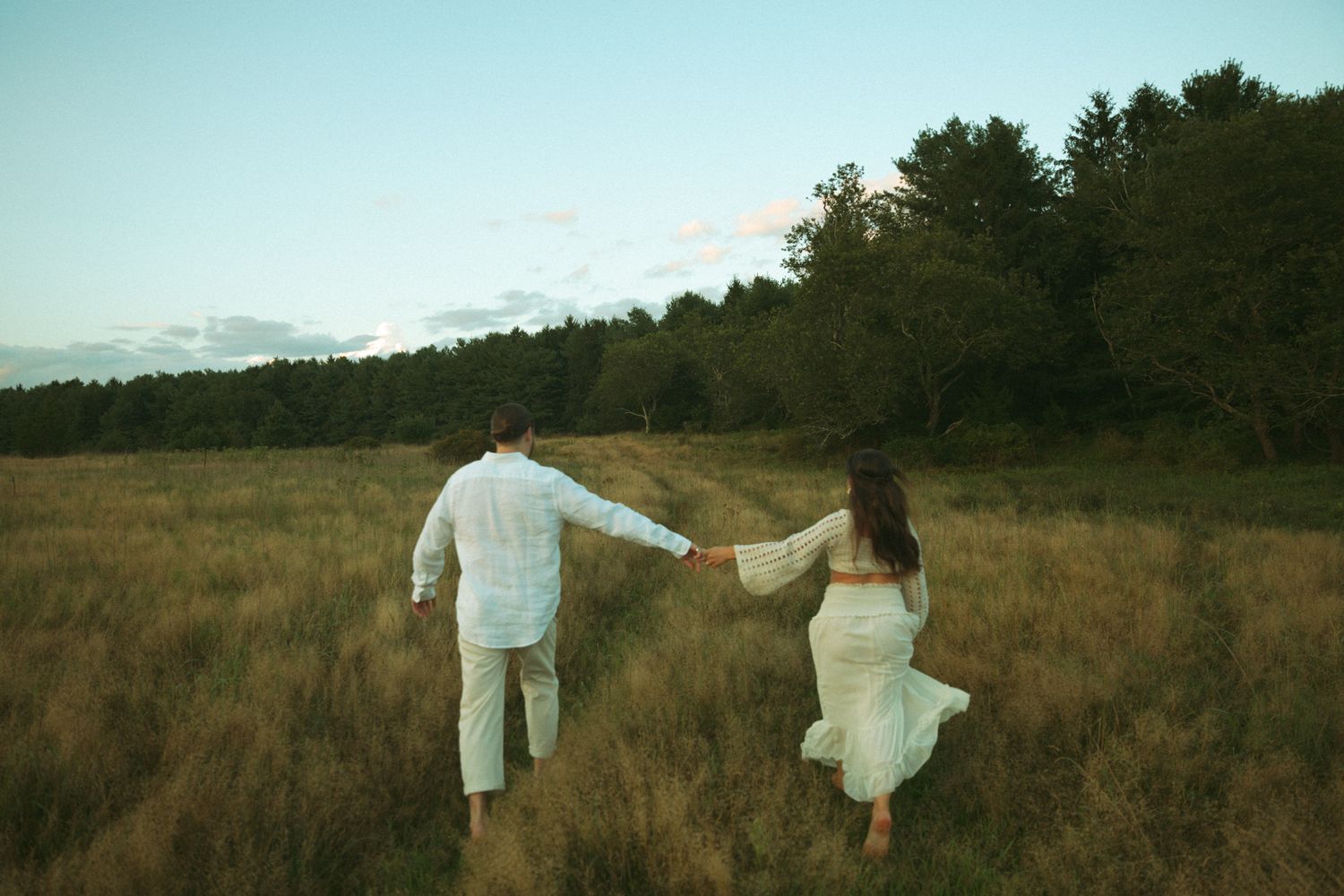 Two people in white outfits dance gracefully across a golden field at dusk.