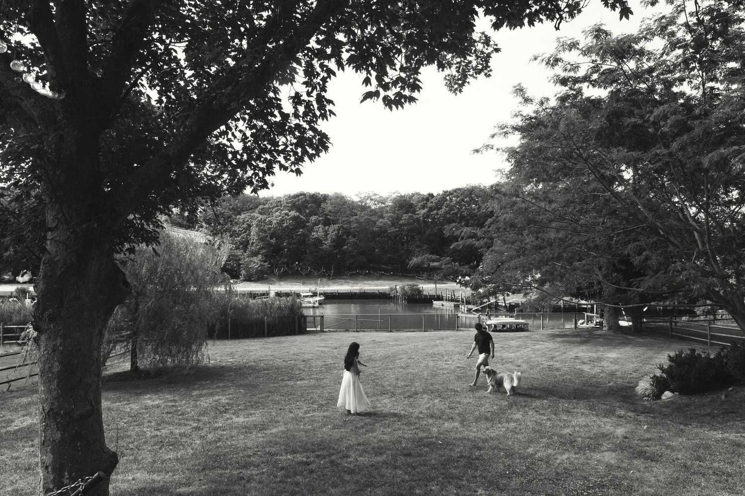 Black and white photo of a child and person walking a dog in a lush green park.