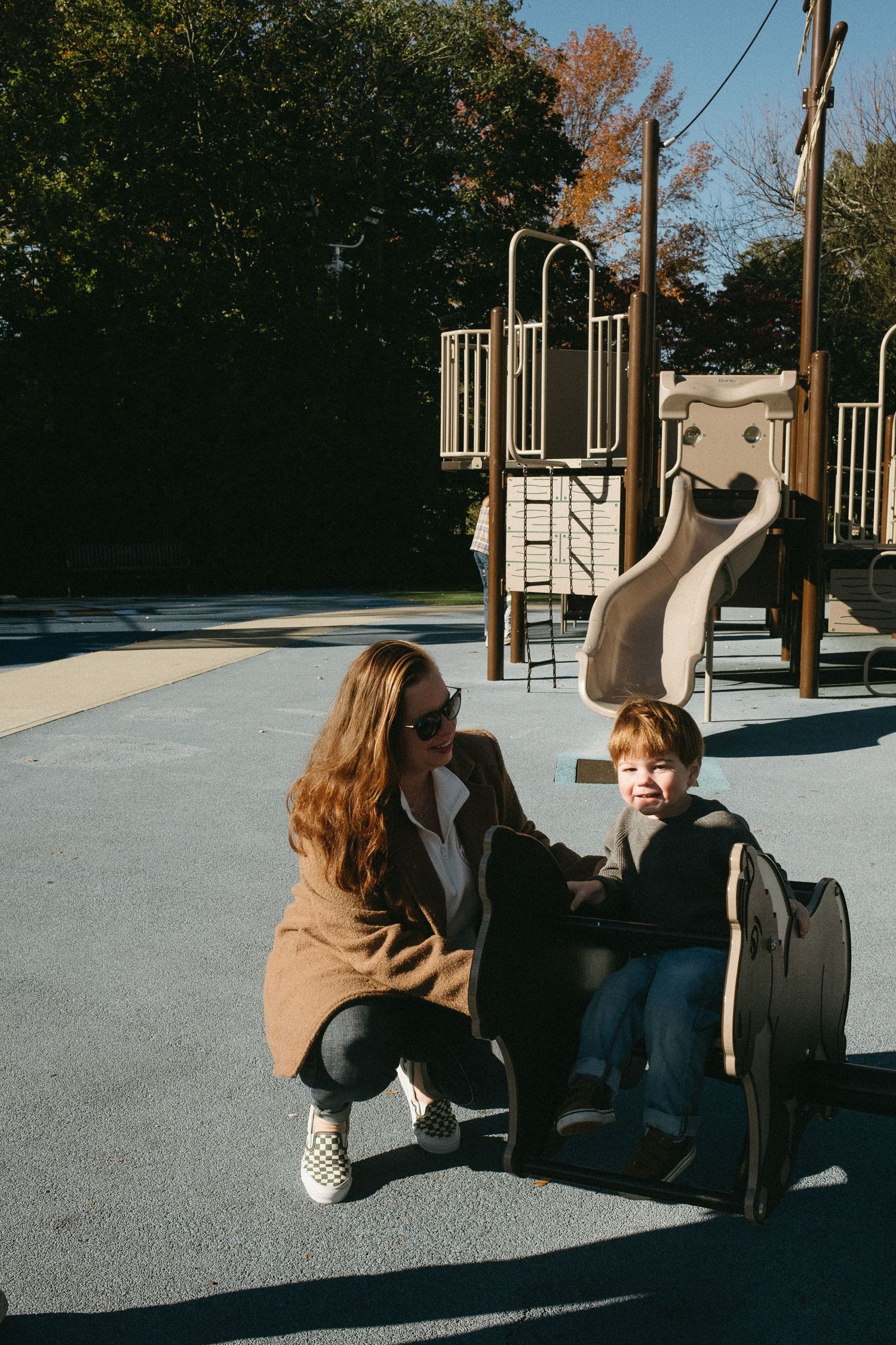 People sitting on playground equipment in a park on a sunny autumn day.