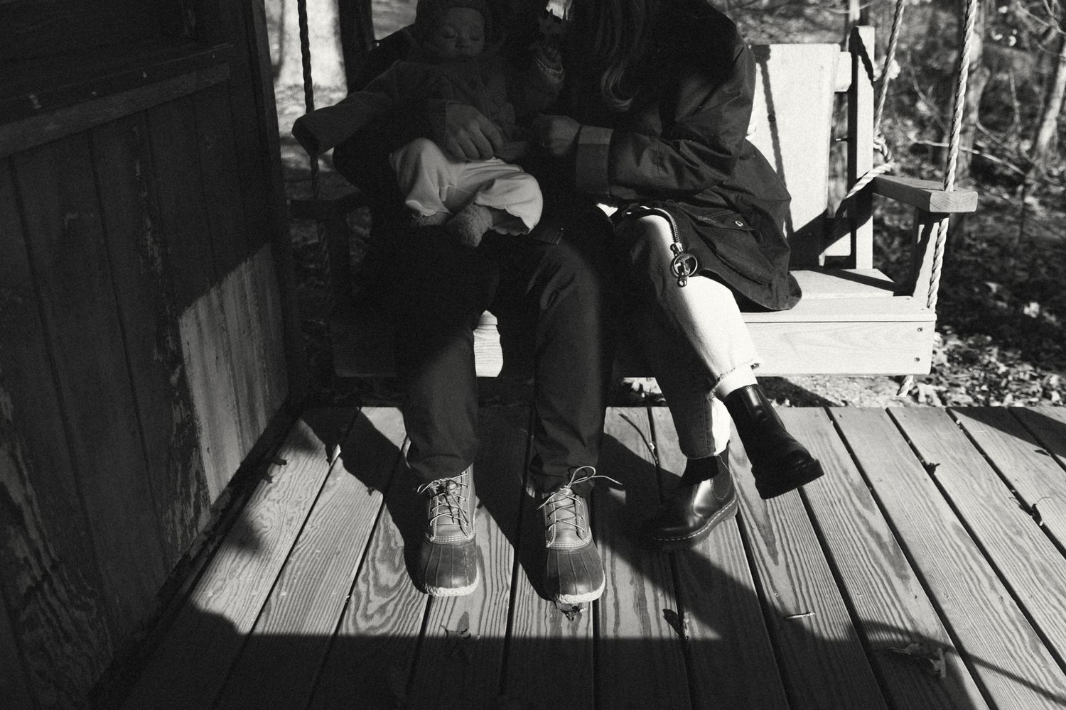Black and white photo showing feet and legs resting on wooden deck boards.