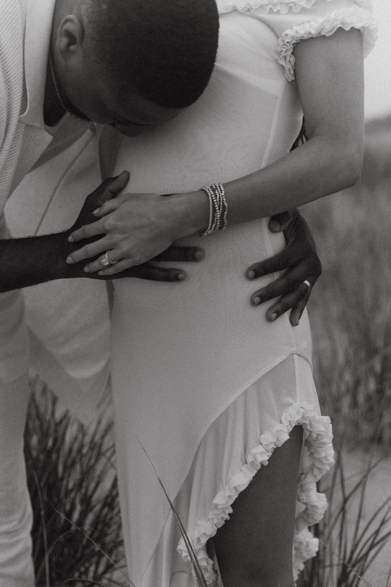 Black and white photo showing intimate embrace with hands on white dress.