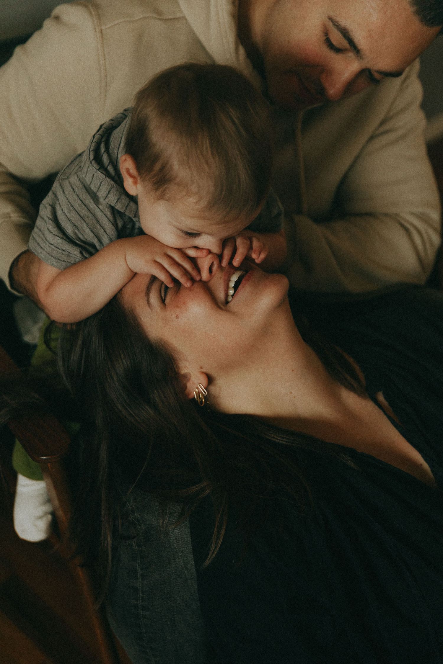 A joyful family moment with a baby touching a smiling mother's face while a father looks on lovingly.