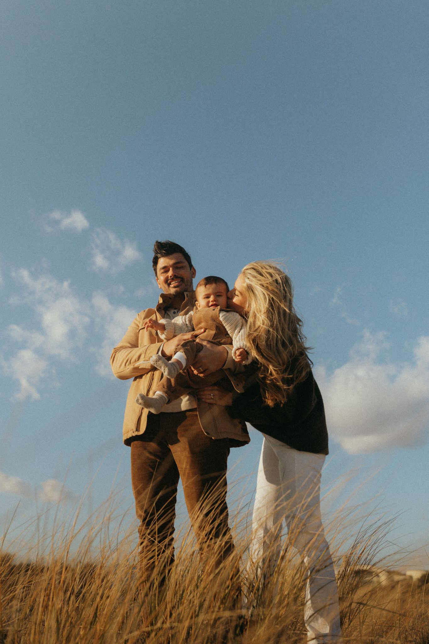 People sharing laughter and embraces in a field of dried grass during golden hour.