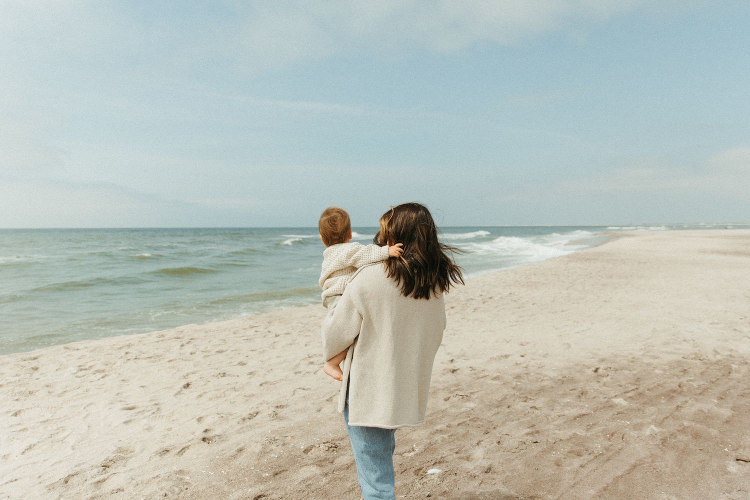 Two people walking along an empty beach shoreline on a sunny day.