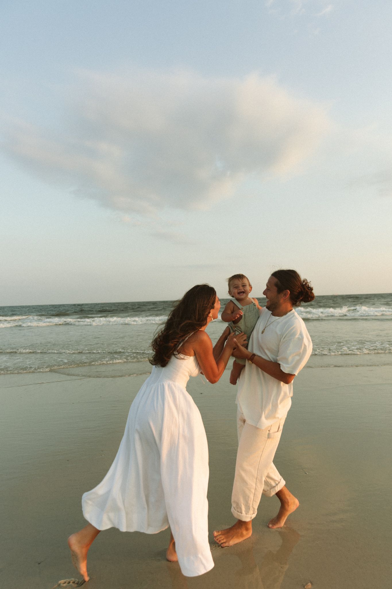 Couple in white clothing dancing together on a beach at sunset creating romantic silhouettes.