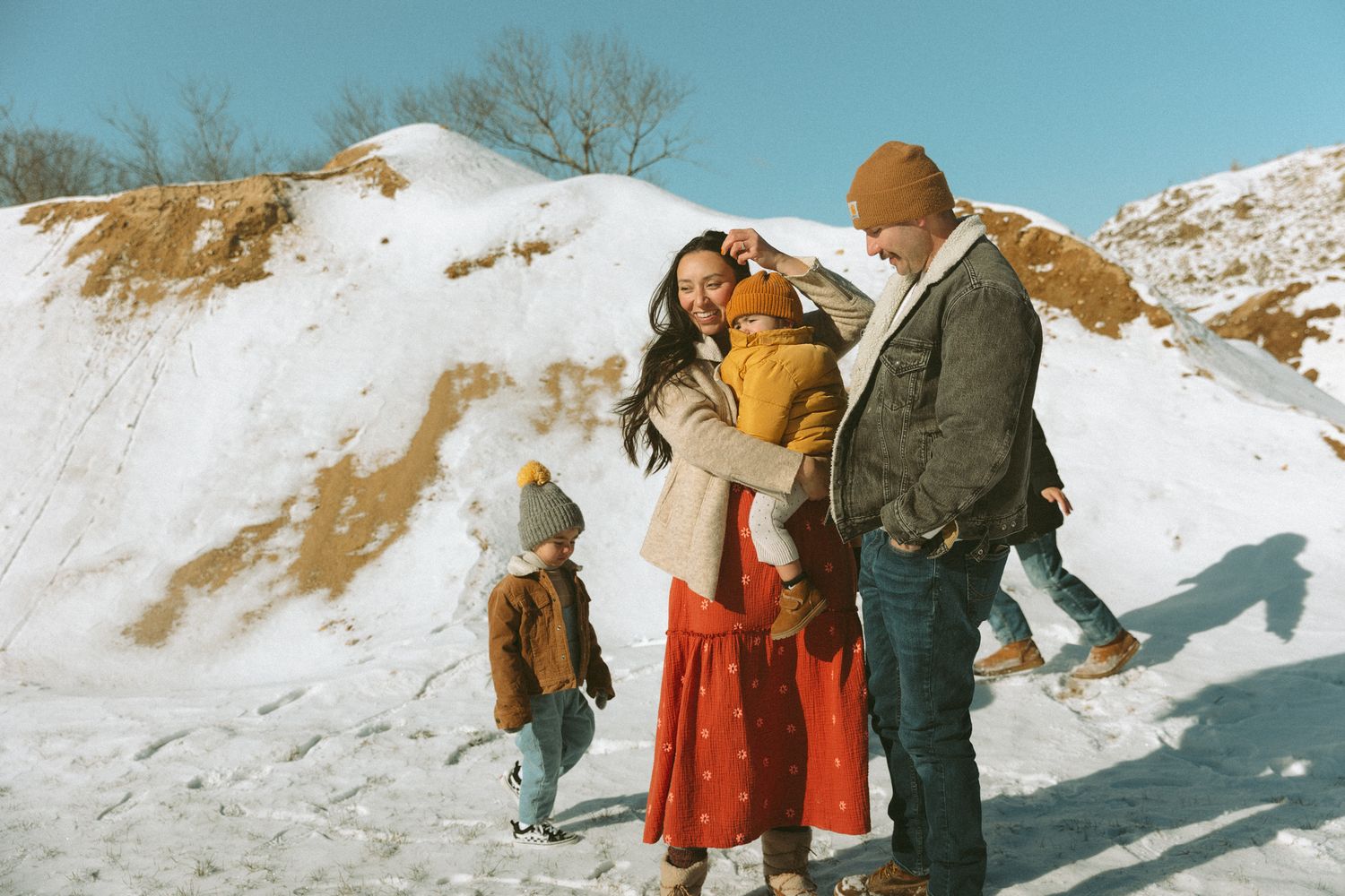 Family of four enjoying a sunny winter day in the snow, wearing warm coats and colorful hats outdoors.