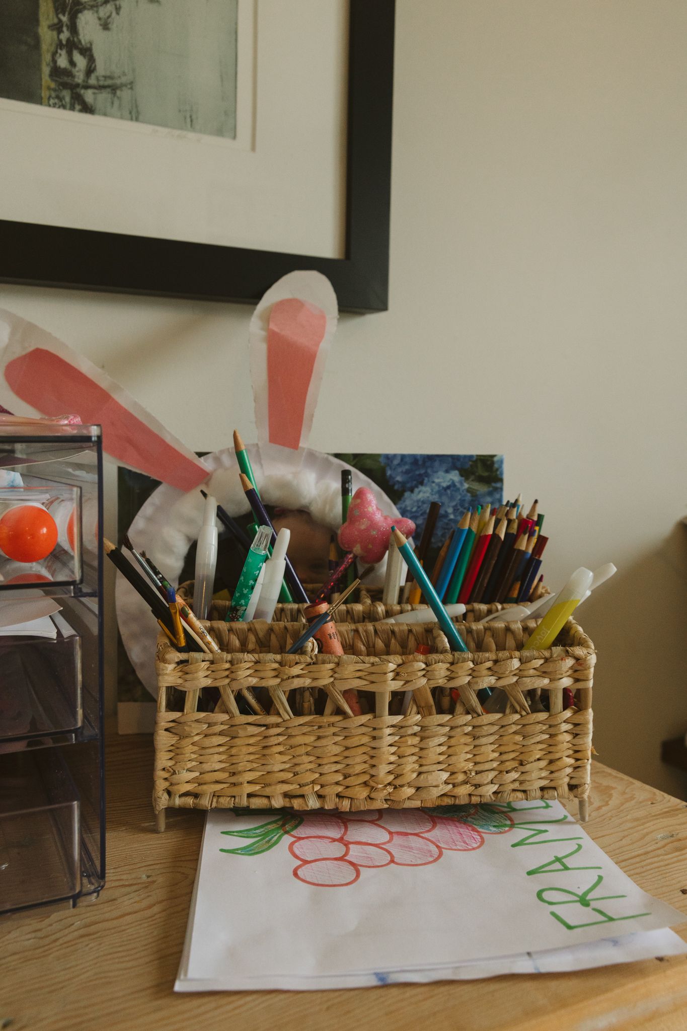 Wicker basket filled with art supplies and colorful markers sitting on a desk.