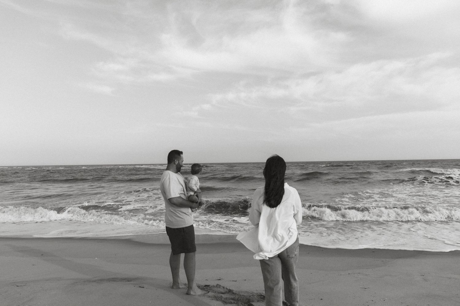 Two people standing on beach looking out at ocean waves.